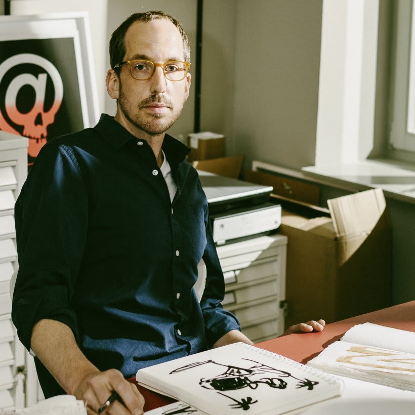 An artist looking into the camera, there is a drawing in front of him