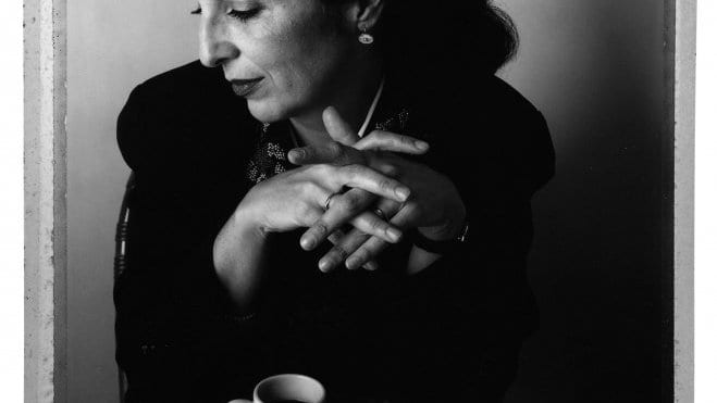 A woman drinks a cup of espressor while sitting at a table.