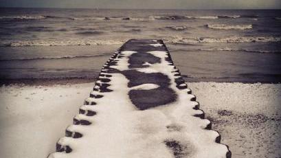 A pier to a large body of water, covered in snow.