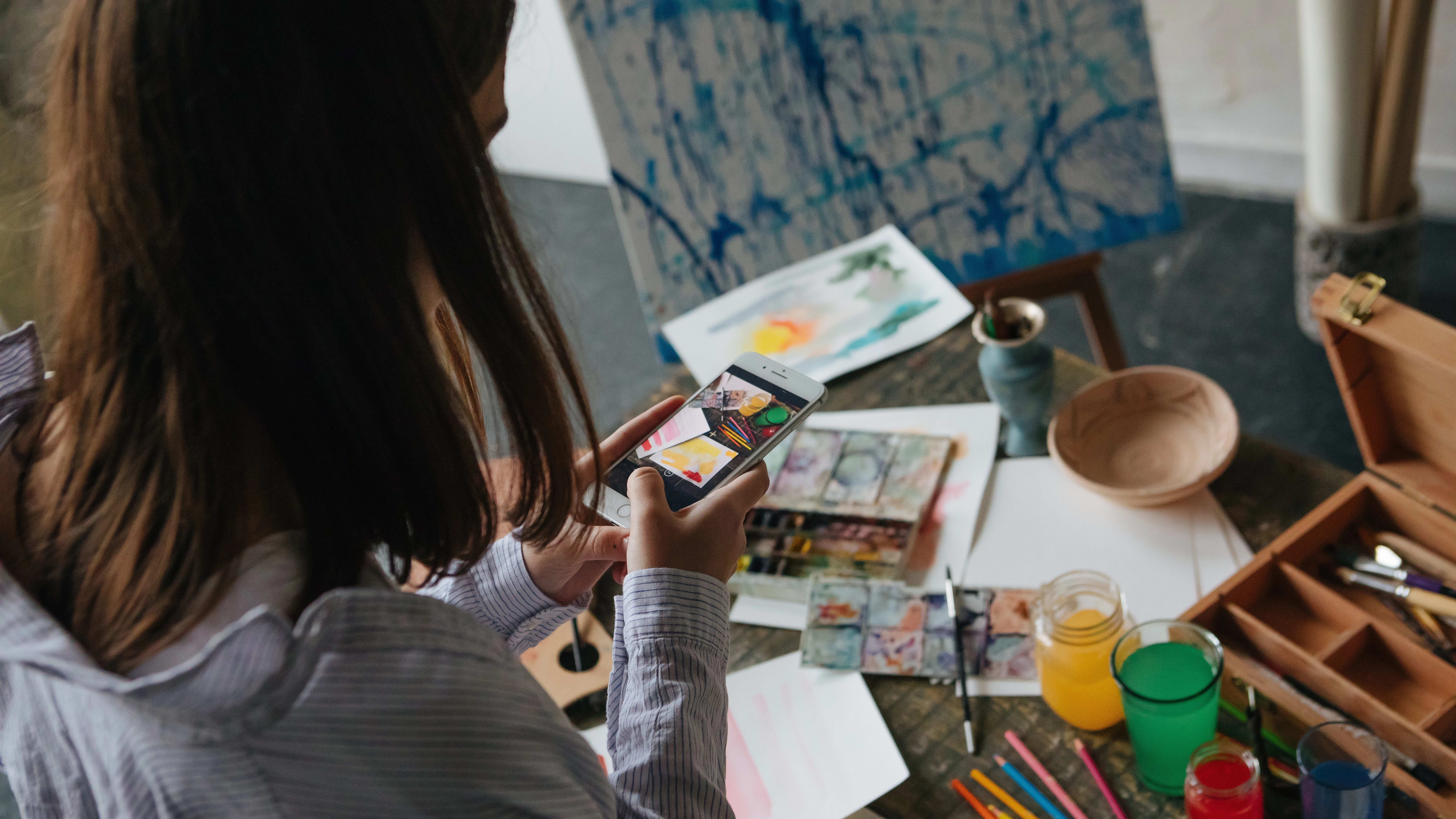 Mobile photos of art. Artist taking photos of her pauntings. Creative work space desk.