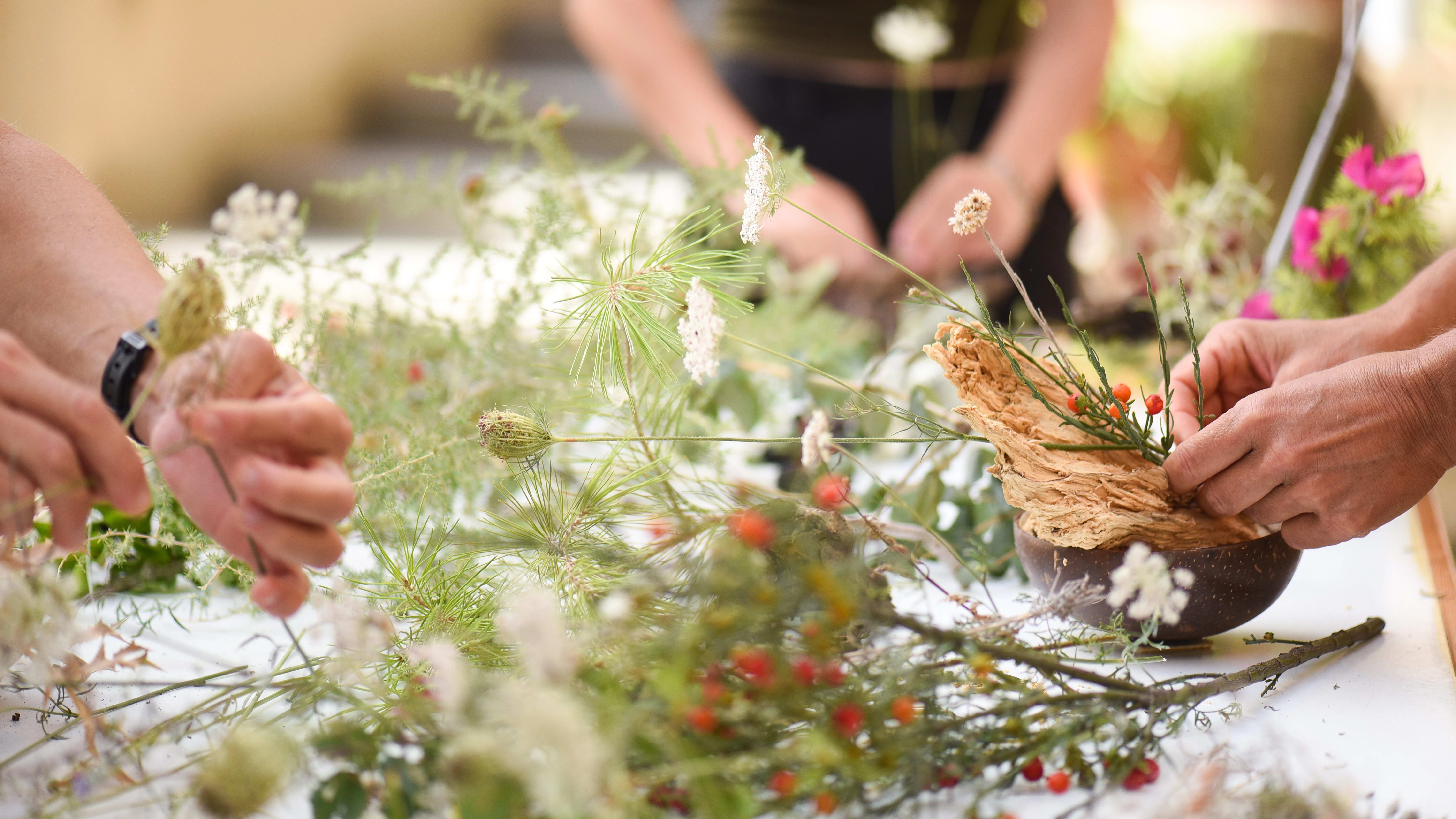 Detail of hands making flower arrangement, outdoor ikebana workshop, different flower arrangements in progress.