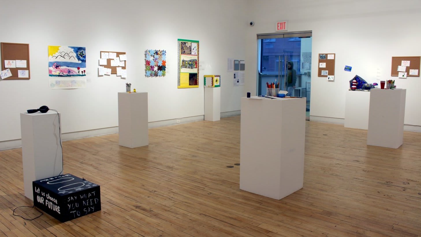 Four bulletin boards covered in cards. Miscellaneous objects displayed on white podiums.