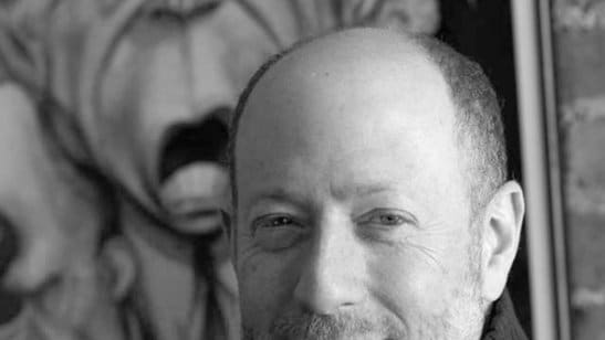 Black and white portrait of Steve Brodner in front of an artwork of his.