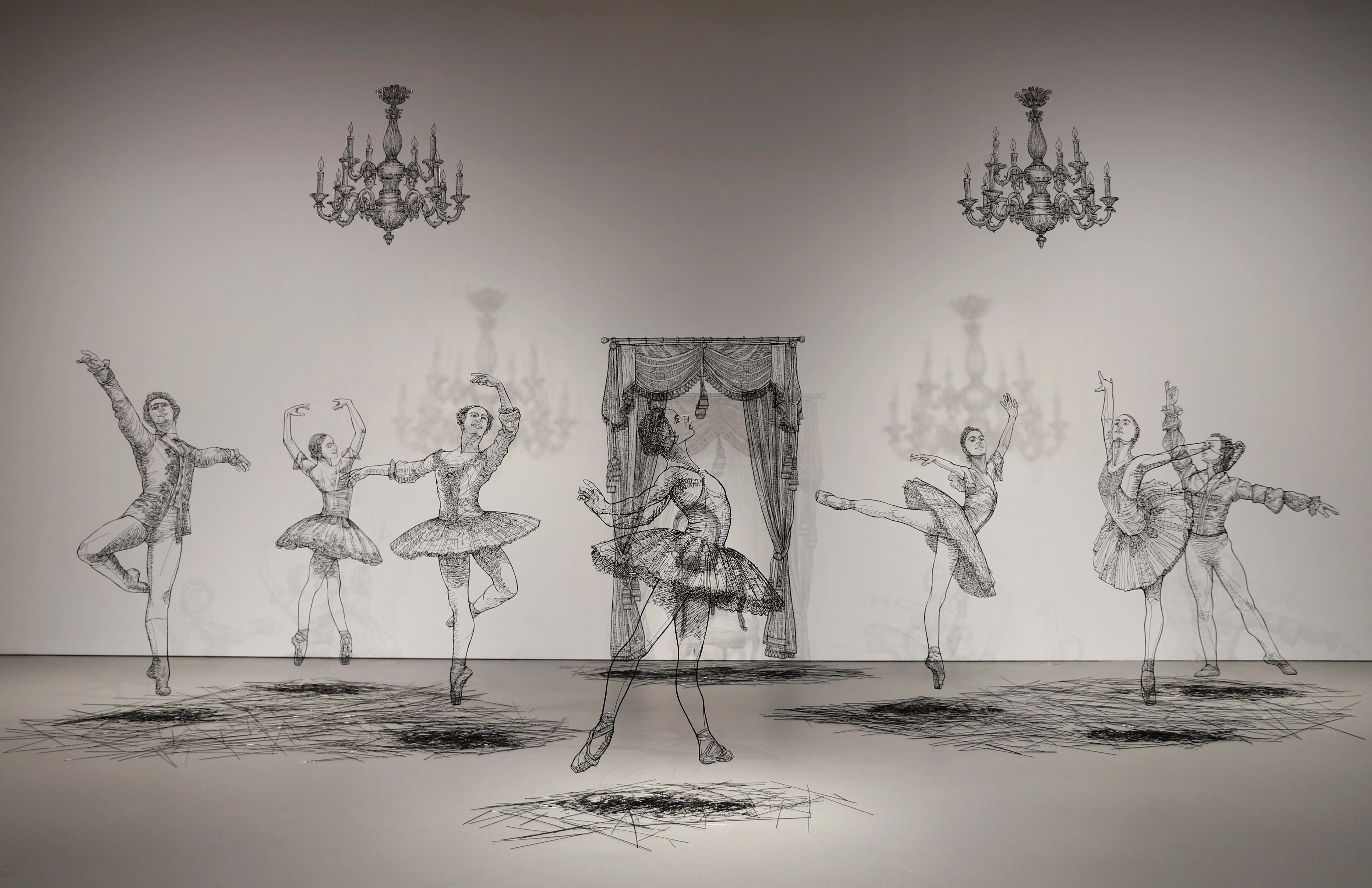 Sculptures made in black wire of several large scale ballerinas dancing around a white room.