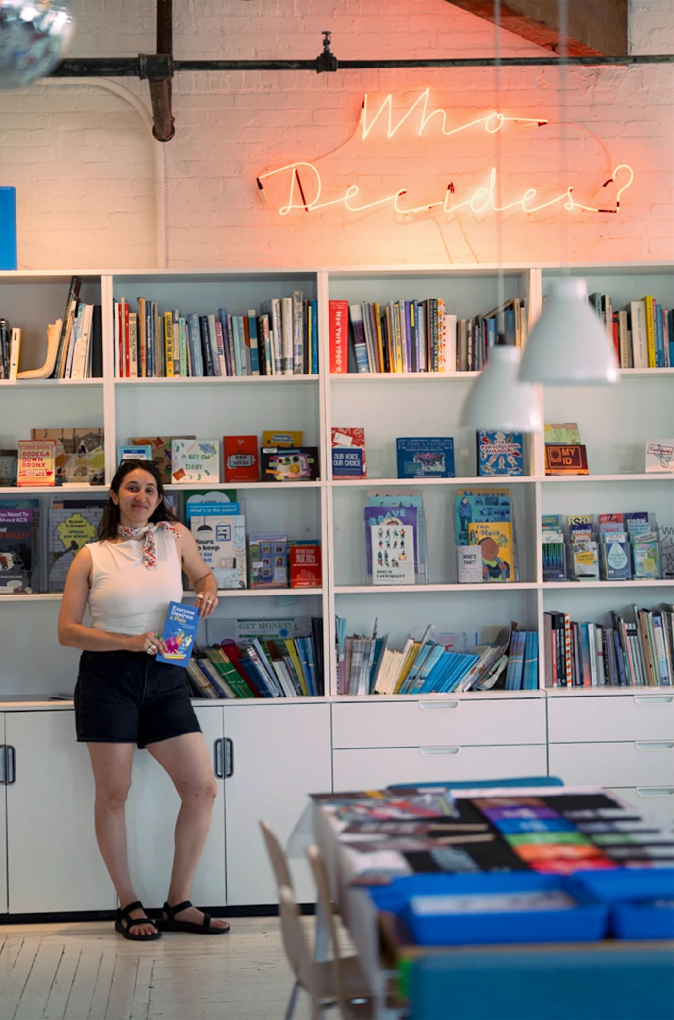 A person in black shorts and a white top holds a book and smiles as they pose.