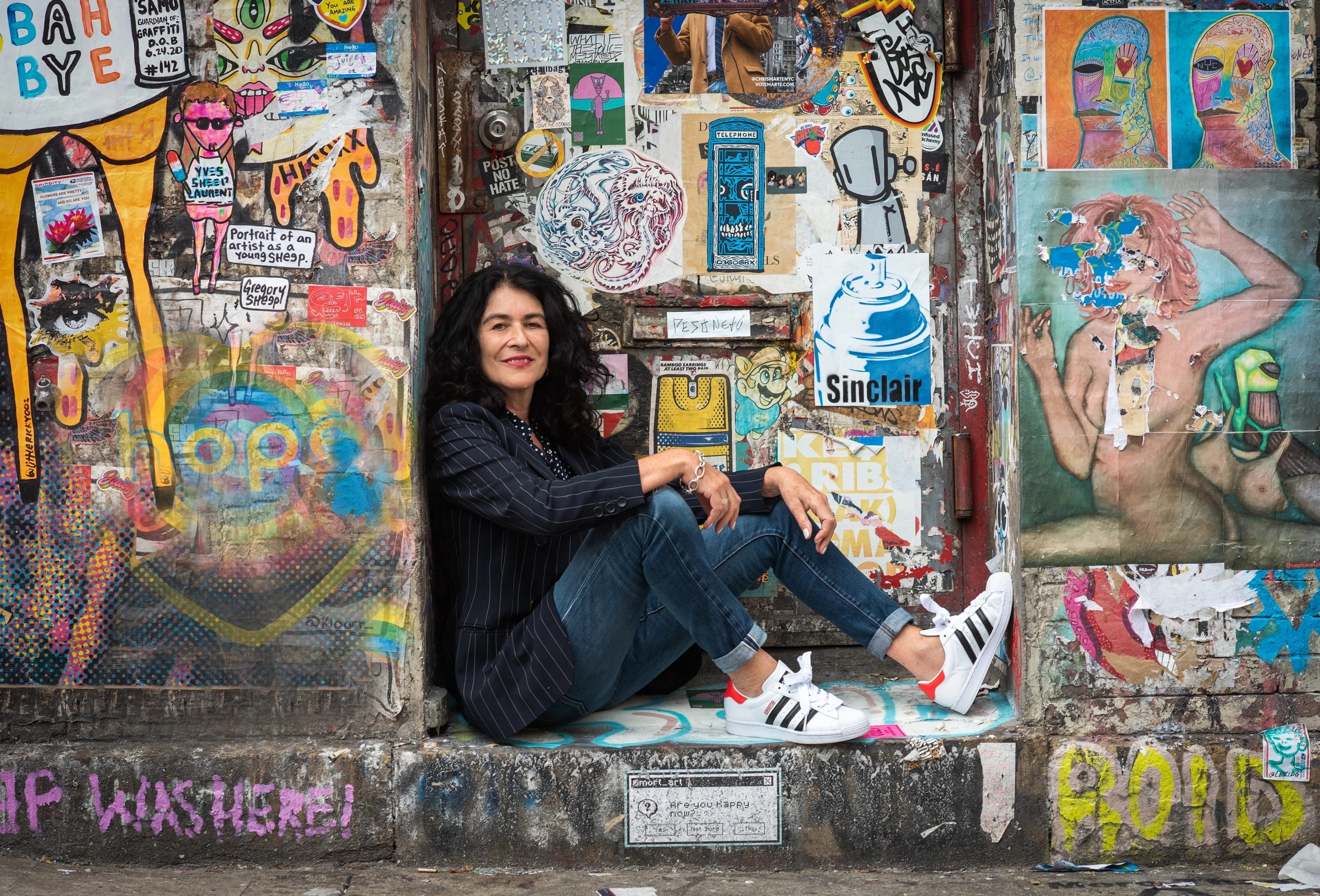 Portrait of photographer Janette Beckman sitting down in front of a graffiti-covered wall