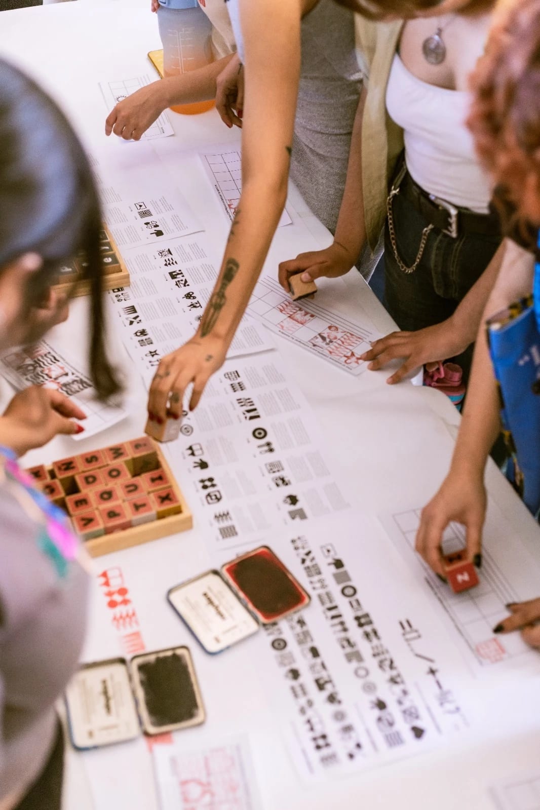 People gather around a table using wooden stamps on paper on a table.