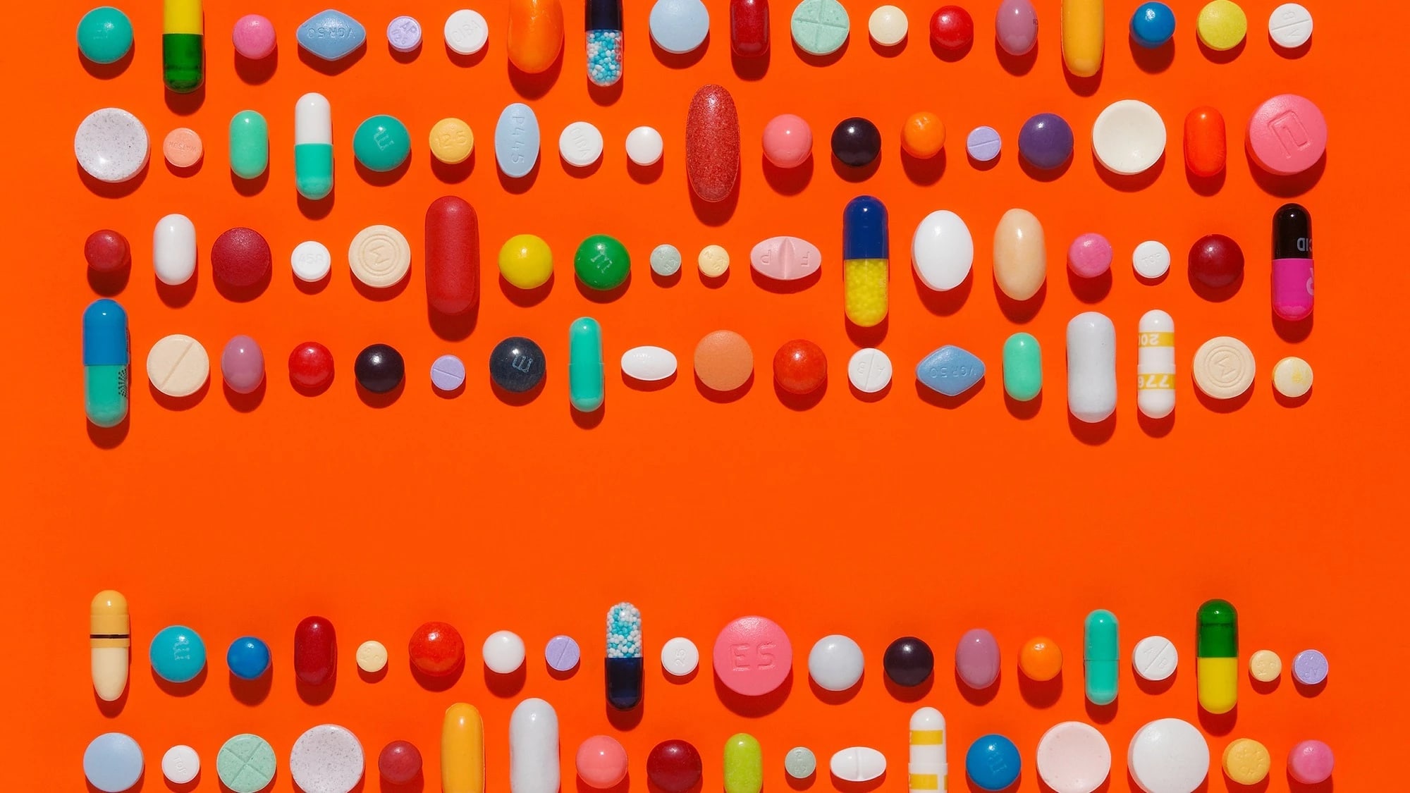 Capsules and pills in a linear composition on a bright orange background.