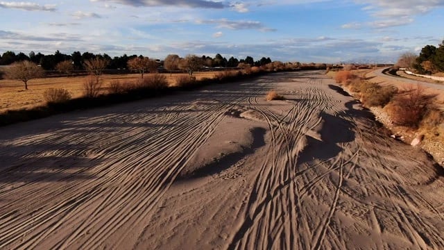 A dry, beige river bed landscape stretching to the horizon with a blue sky of the Rio Grande 