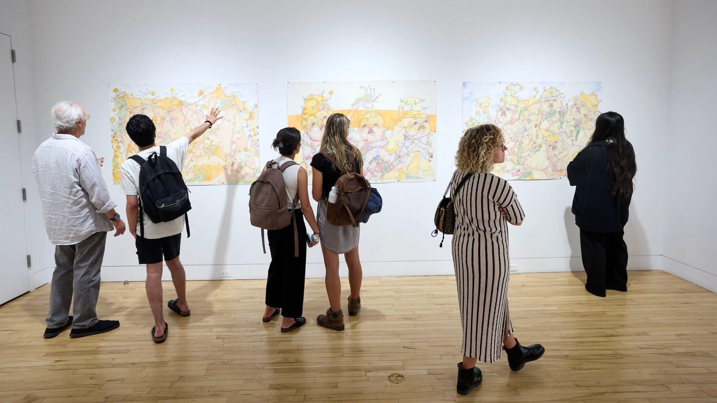 People in gallery look at three drawings on wall