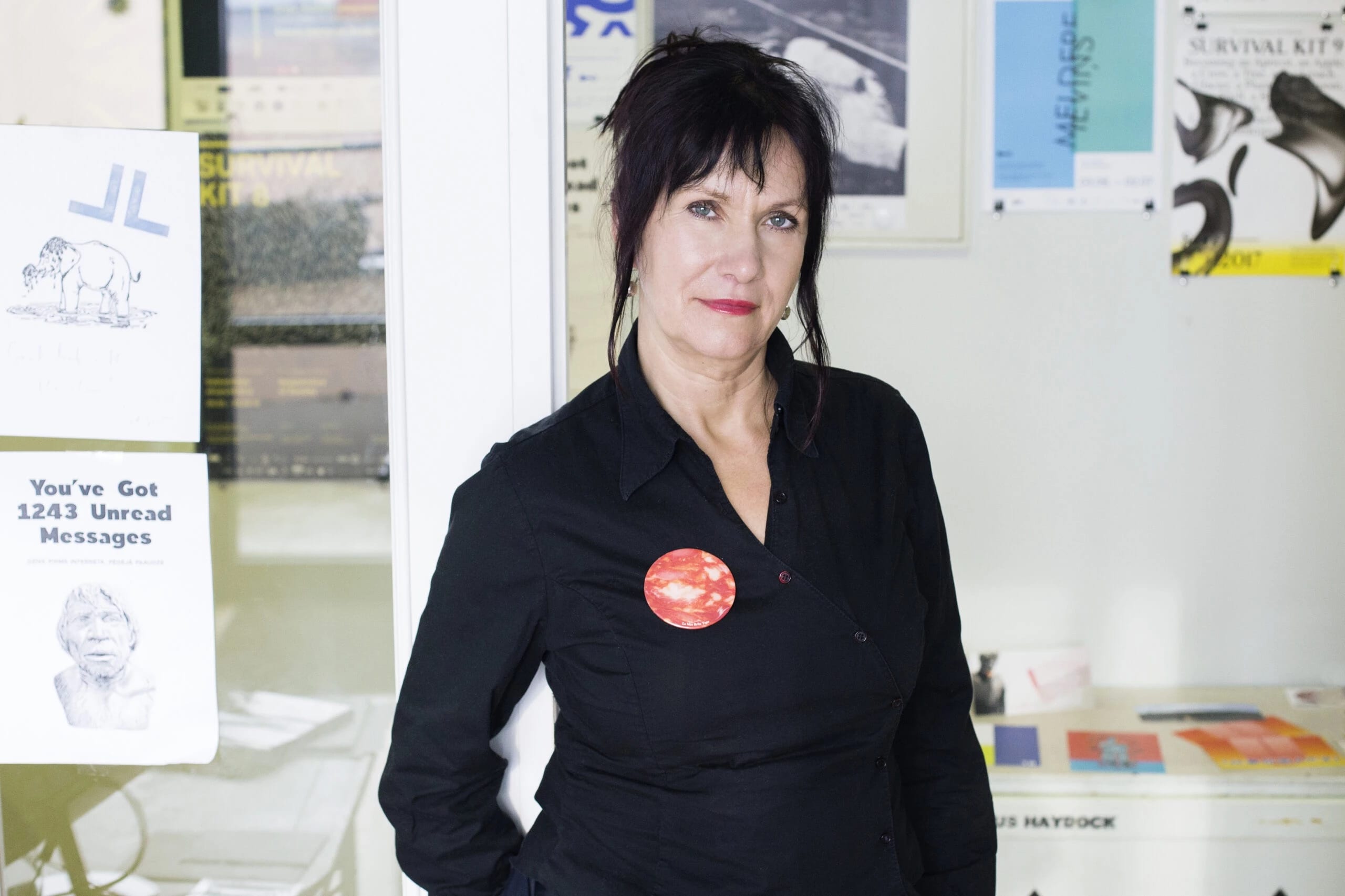 A person in a black button up shirt with red and blue buttons in white room decorated with posters