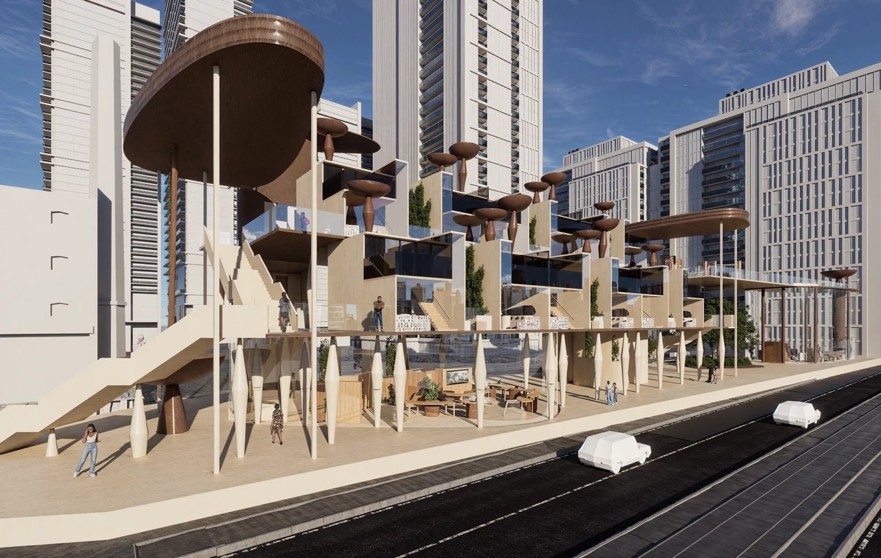This image shows a futuristic, multi-level architectural structure with sculptural wooden forms and glass-walled spaces set against a backdrop of tall modern buildings. Walkways, terraces, and elevated platforms create an open, layered environment where several people are moving through the space.