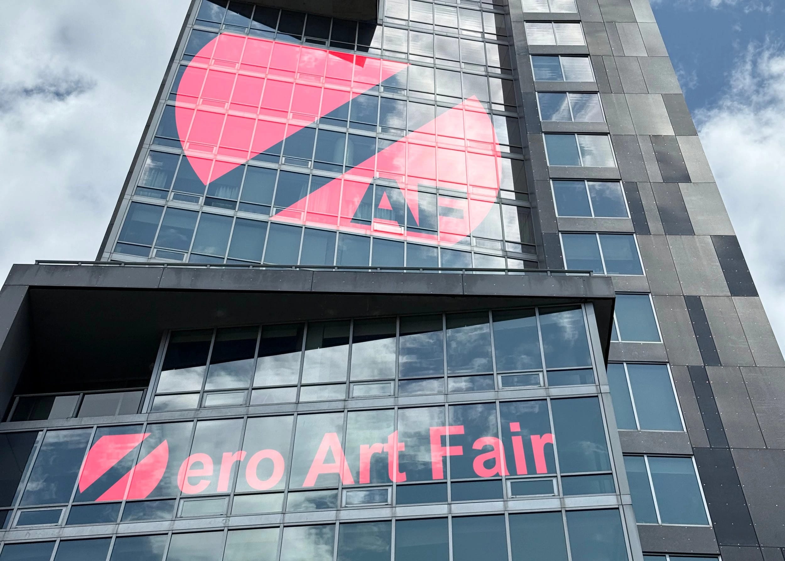 A modern skyscraper facade with the Zero Art Fair logo displayed in its windows.