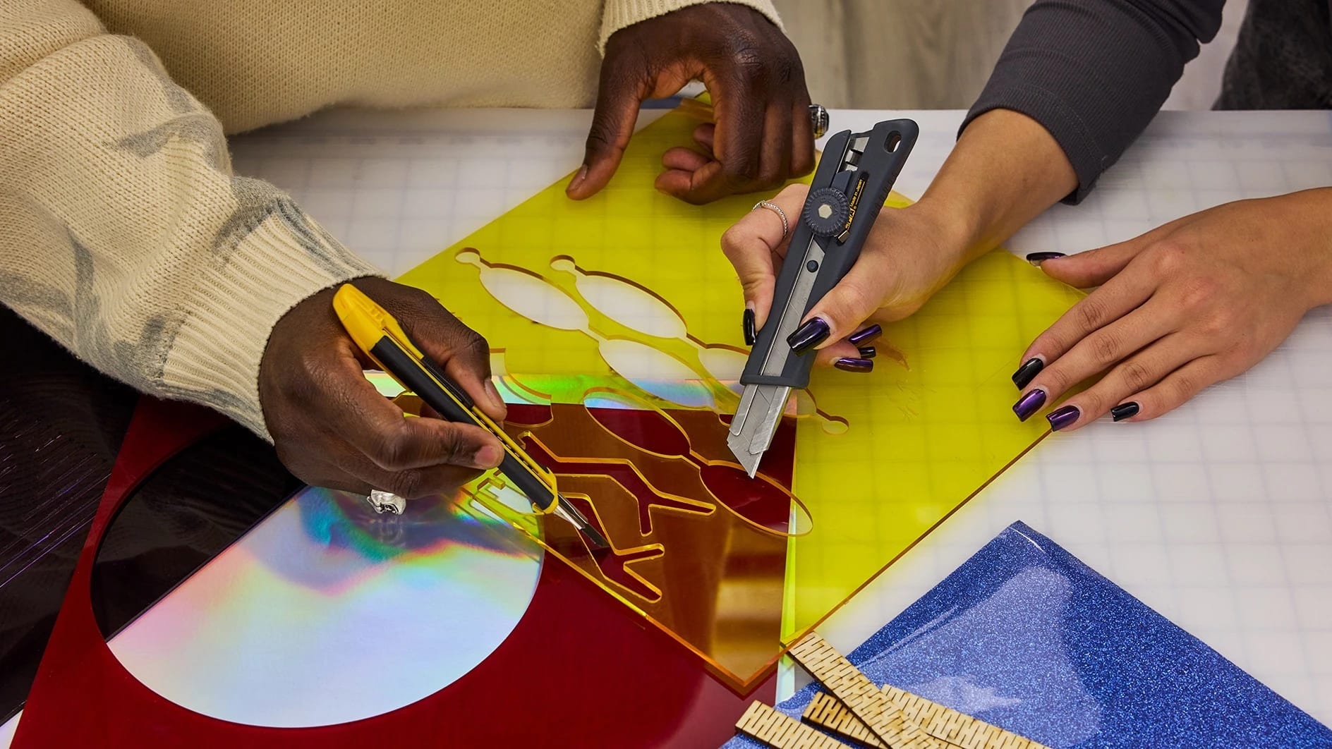Overhead view of two student's hands cutting elaborate shapes out of colored plaxiglass on a work surface