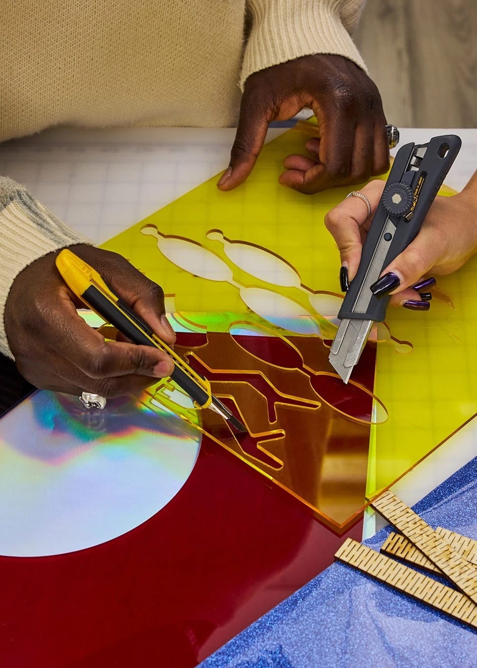 Overhead view of two student's hands cutting elaborate shapes out of colored plaxiglass on a work surface