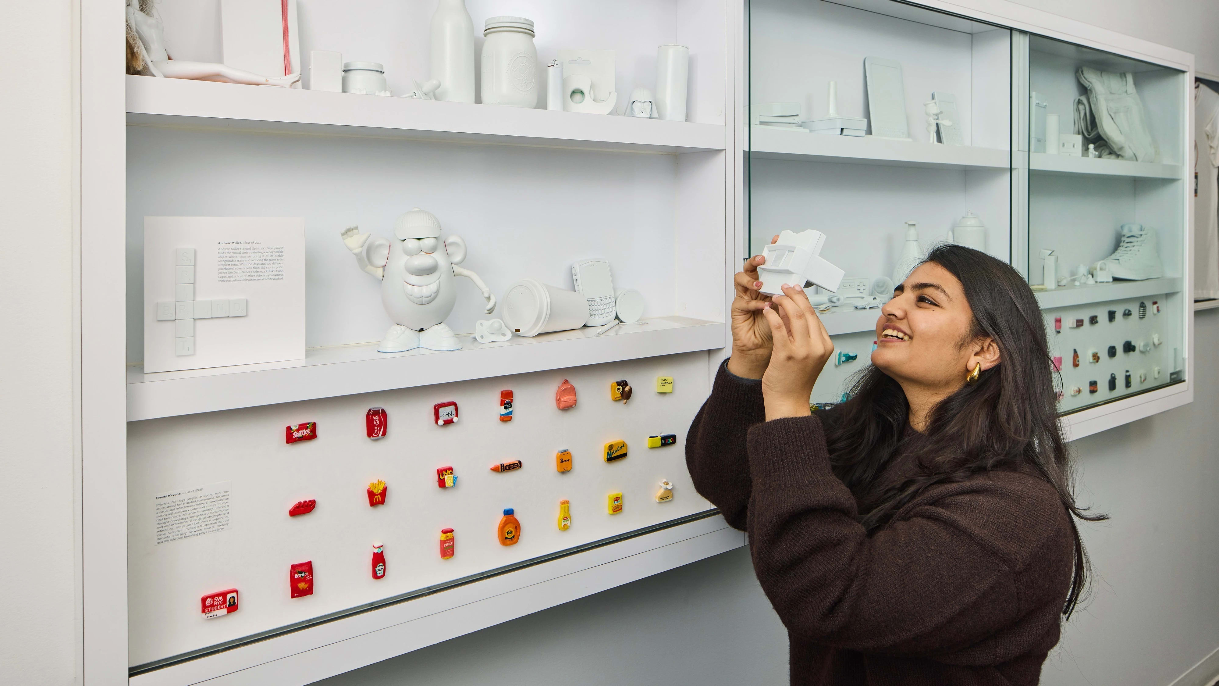 Female student looking into a vintage viewfinder in front of shelves of branding objects all painted white