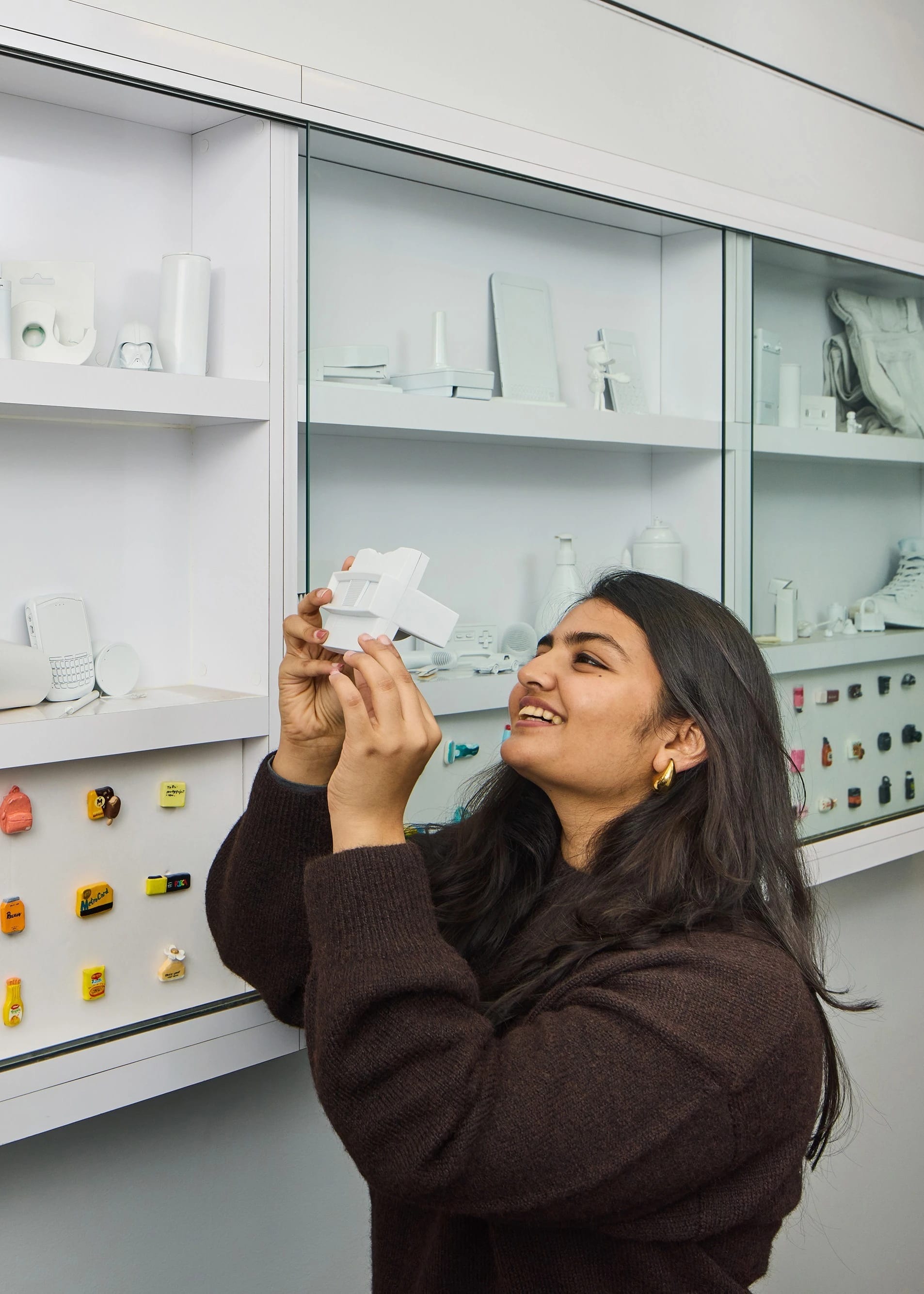 Female student looking into a vintage viewfinder in front of shelves of branding objects all painted white