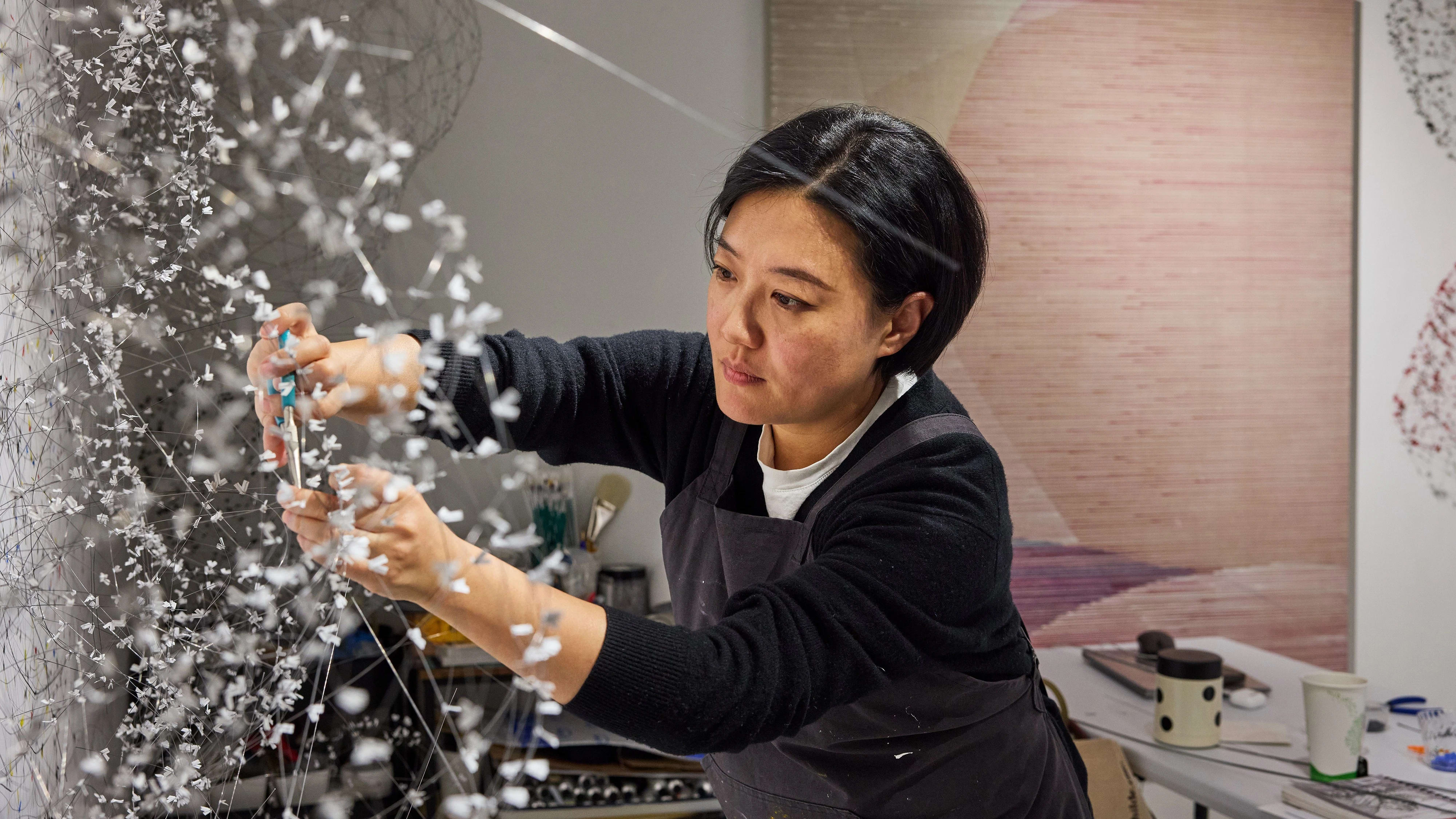 Female artist working intently on a large-scale elaborate wire sculpture in her studio