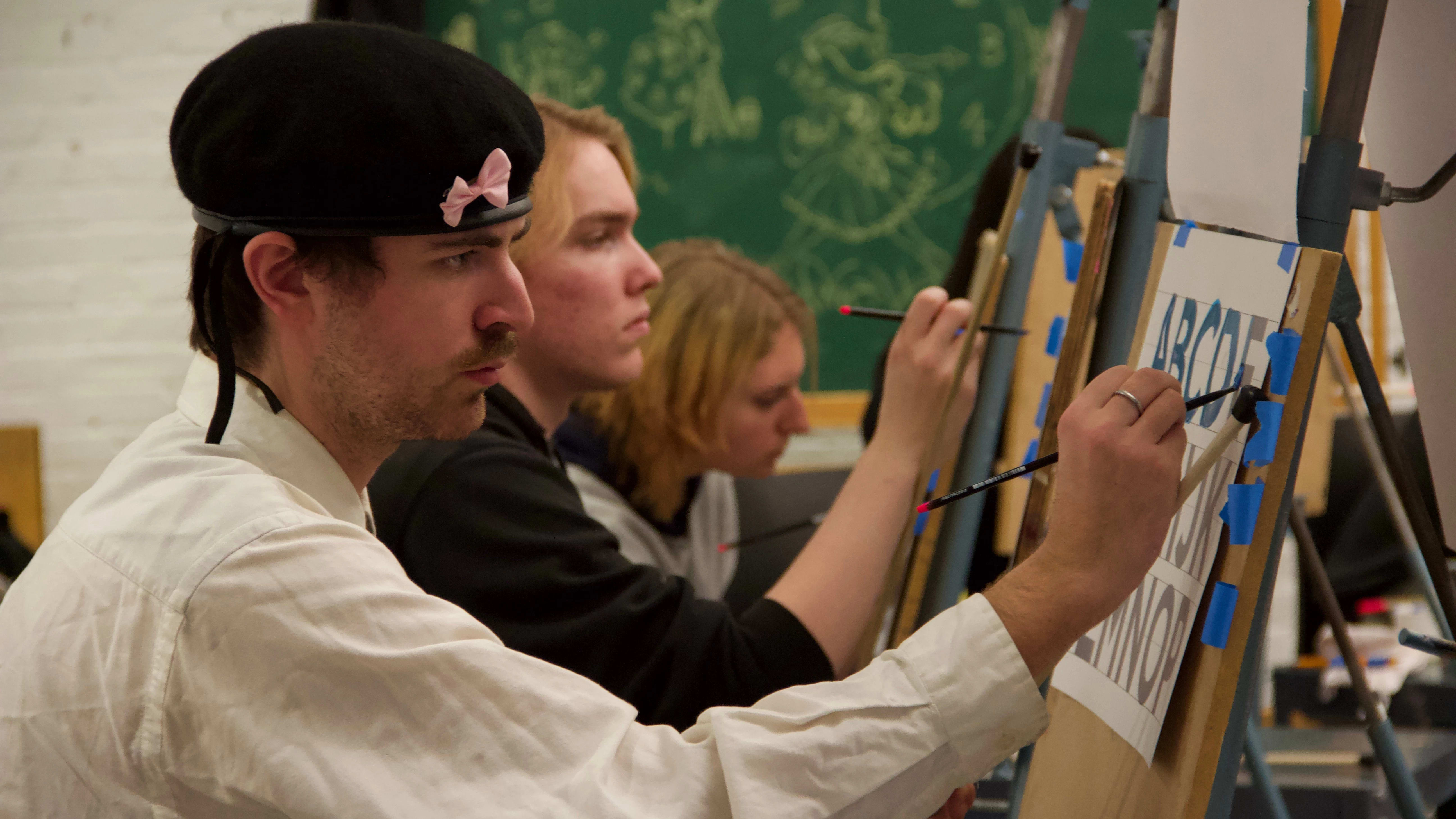 Students working with pencils on easels in a hand lettering class.