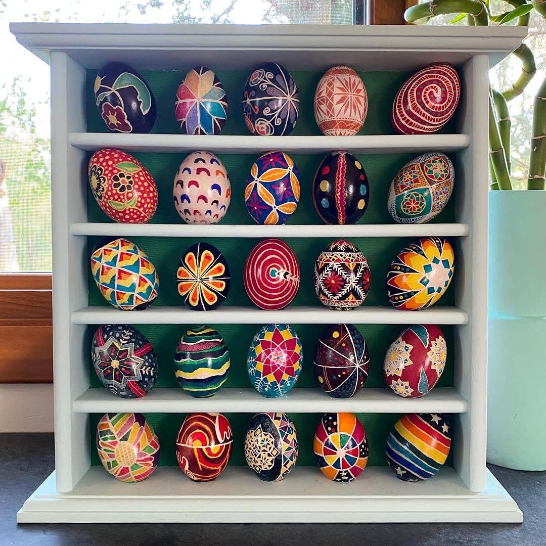 25 colorful Ukrainian Easter eggs lined up on a bookshelf.