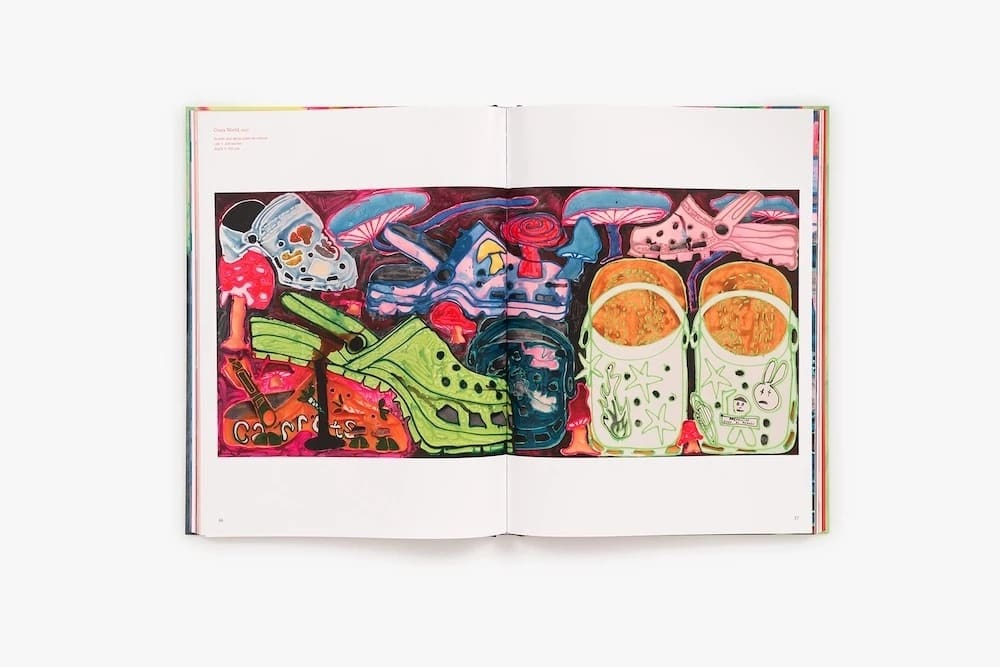 A photograph of a book open to a layout reproducing a colorful painting of several pairs of Croc shoes interspersed with mushrooms