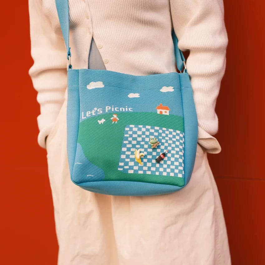 a peron in a white outfit with a blue tote bag stands against a red wall