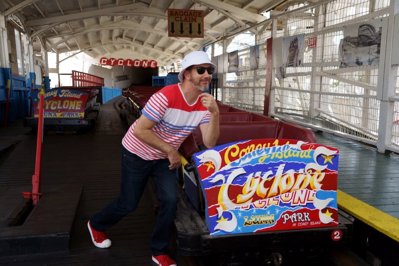 Steve Ellis poses happily next to the Coney Island Cyclone roller coaster car, which features his illustration on the front panel.