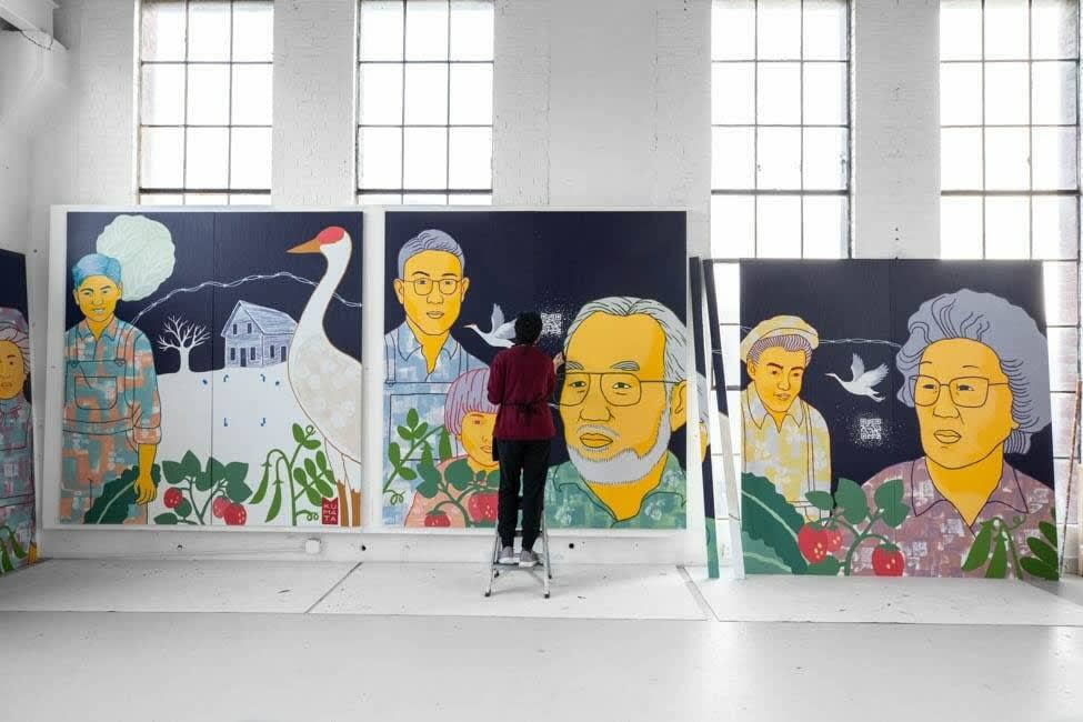 A photograph of a large, multi-panel mural with an artist working on it.