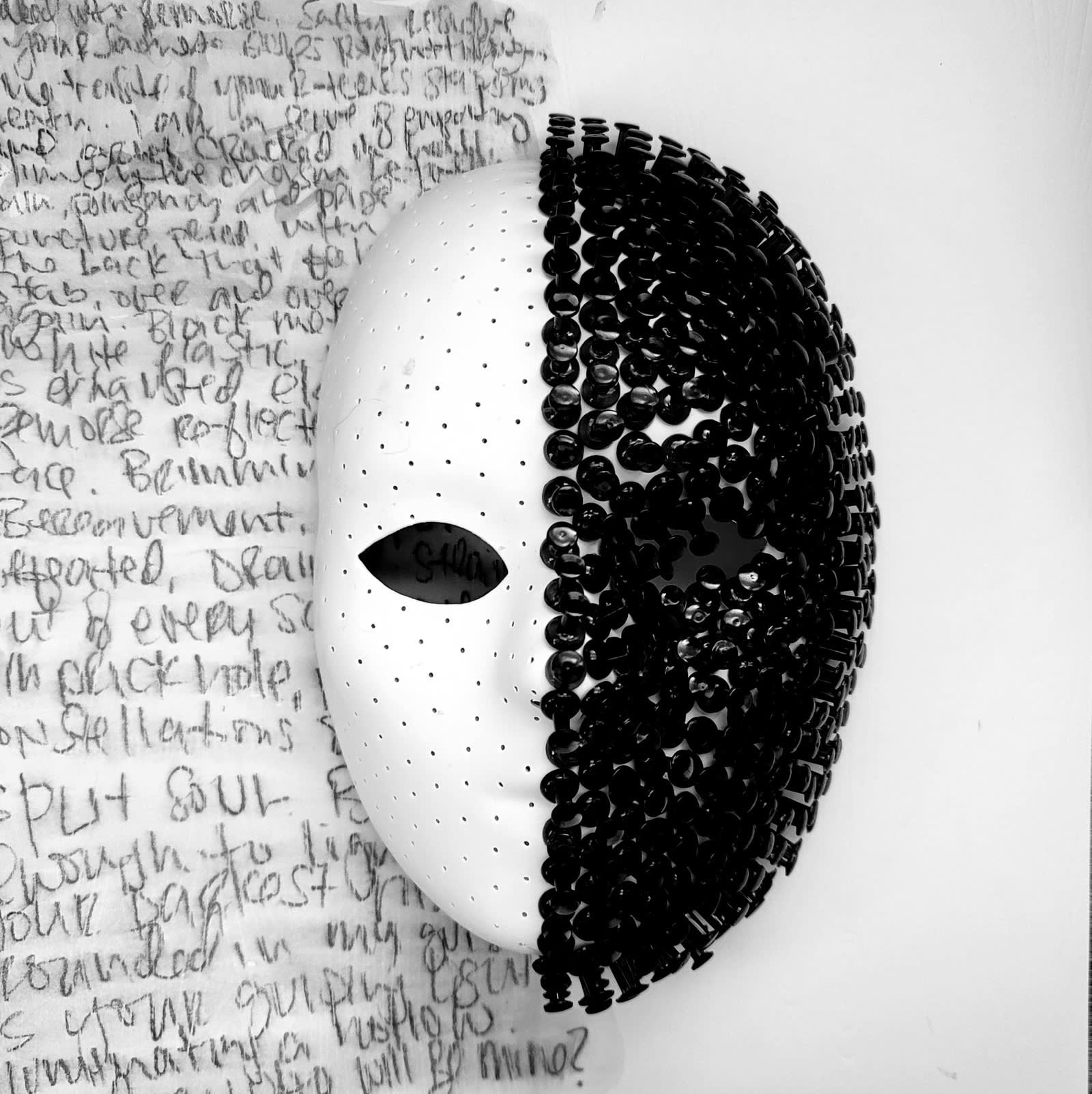 A mask that is white with small holes in one side and covered in black push pins on the other side