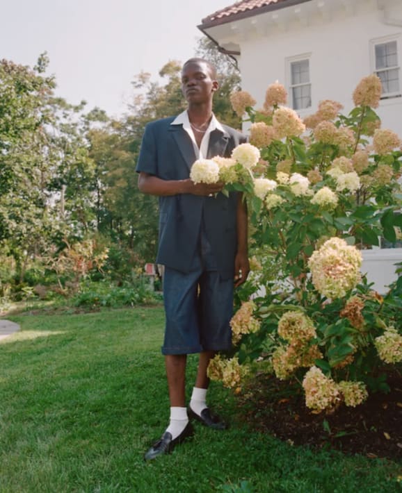 A photograph of a person standing next to a flowering plant.