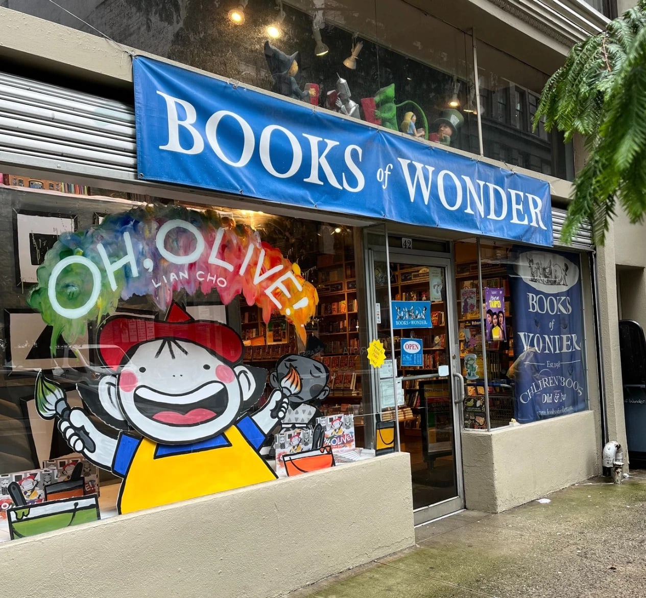 The Books of Wonder storefront with a window display of an illustrated boy in a red cowboy hat saying "Oh oliver"