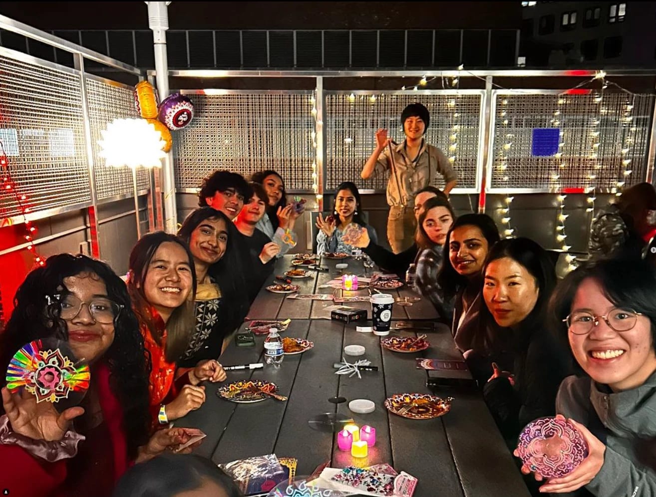 A group of students sit at a table on a roof with plates of food in front of them