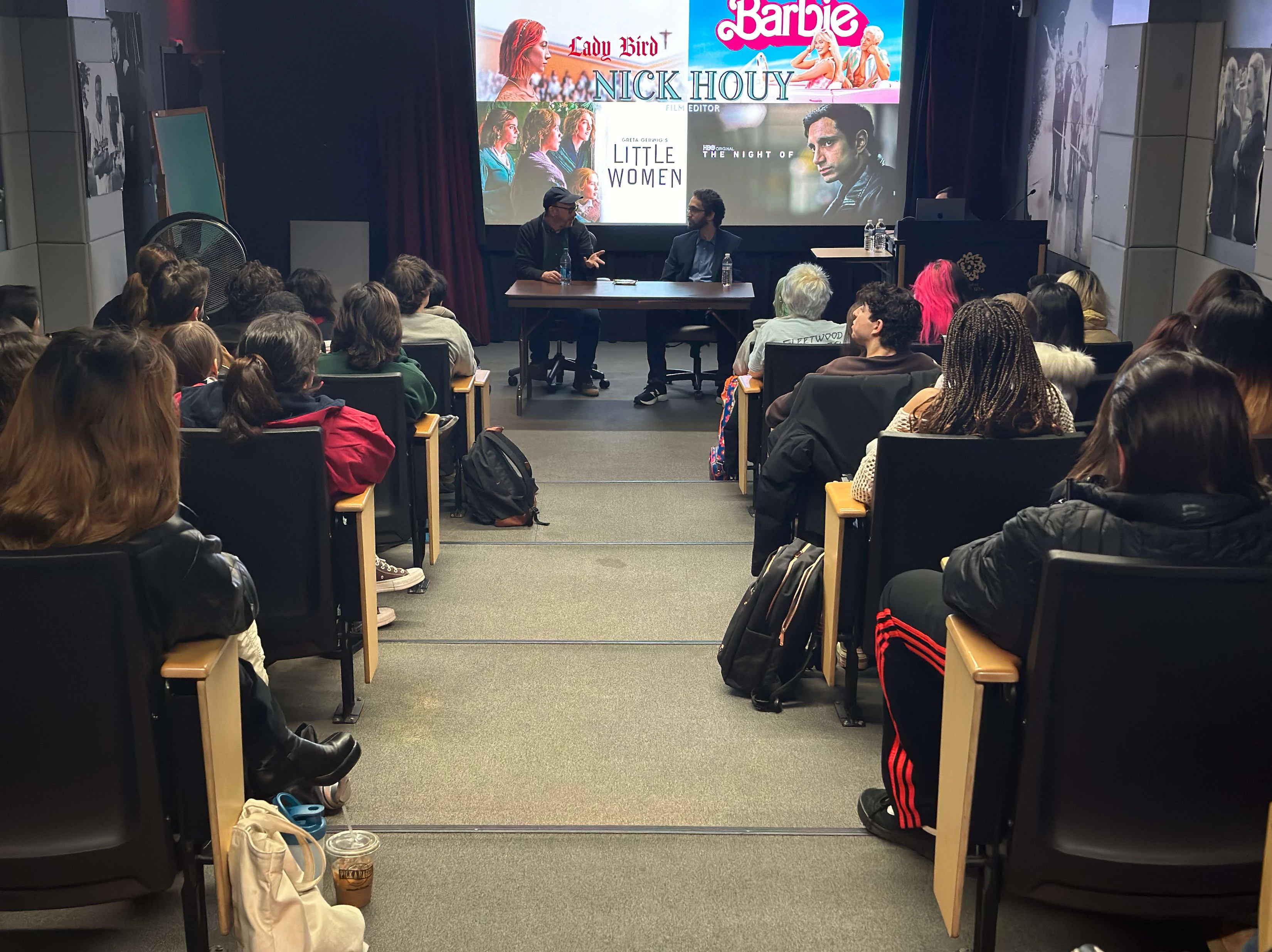 A room full of people watch two speakers at the front who are presenting with visuals behind them