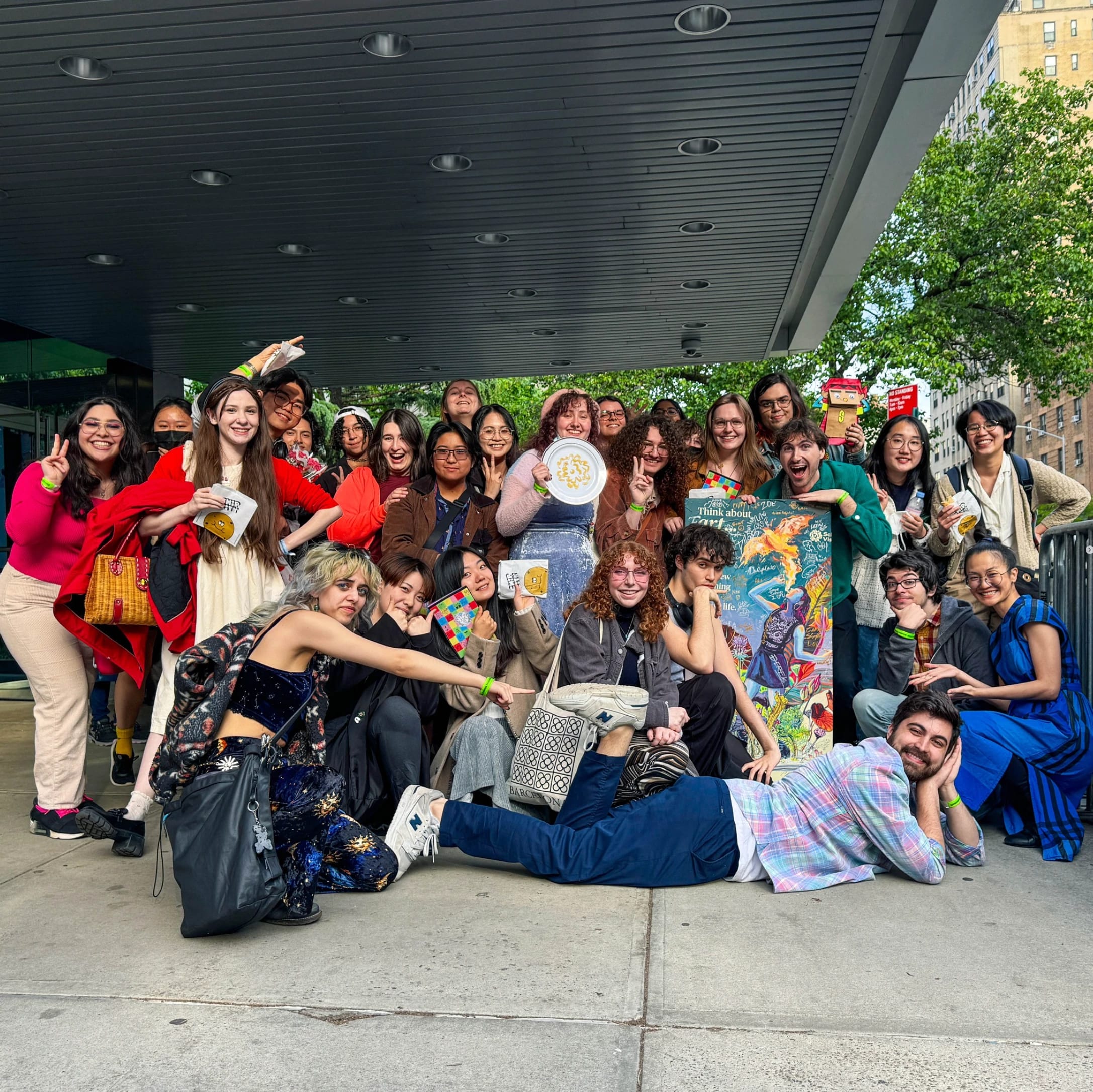 A group of students pose outside of the SVA Theatre holding various signs and merch 