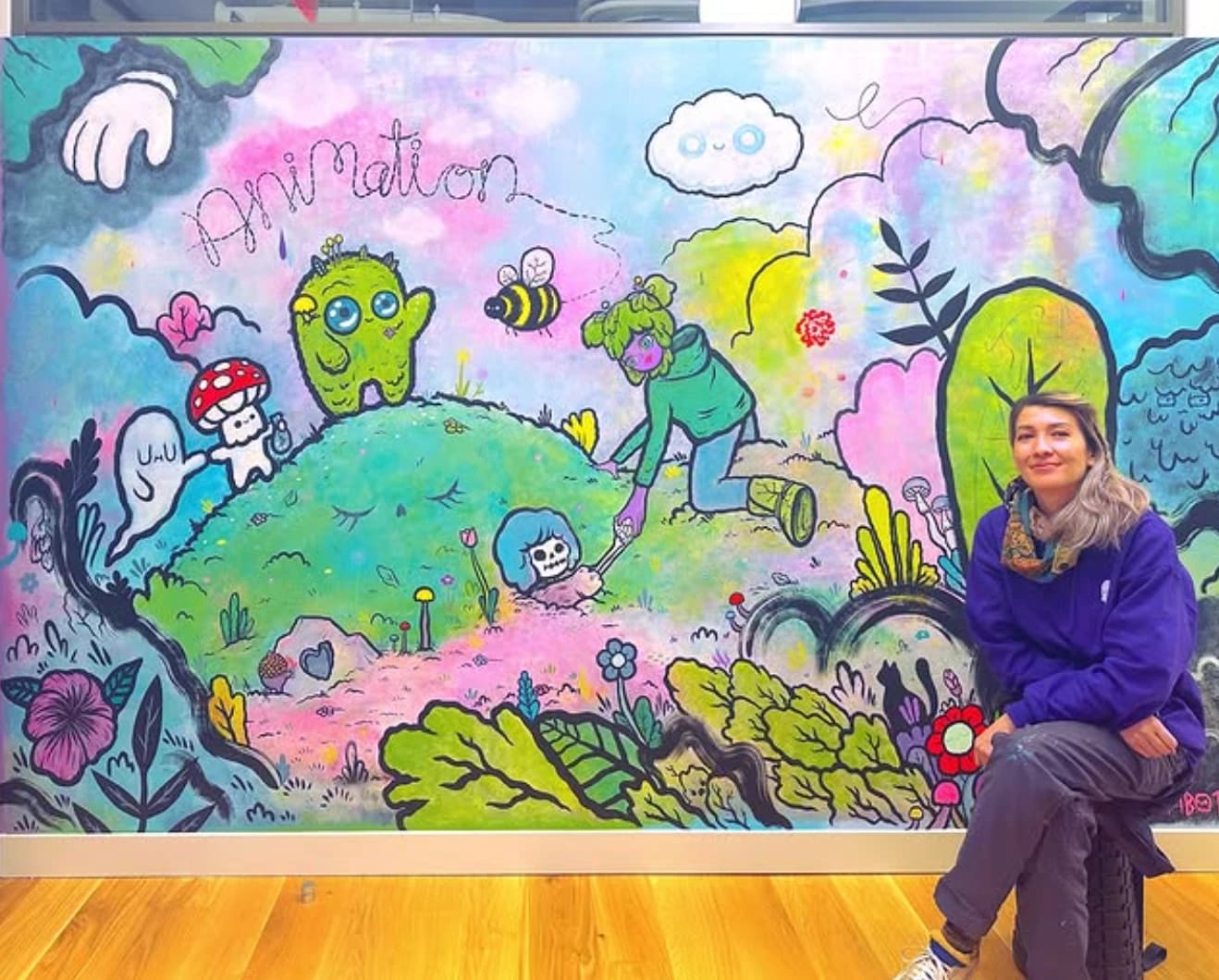 a woman sits smiling in front of a colorful mural