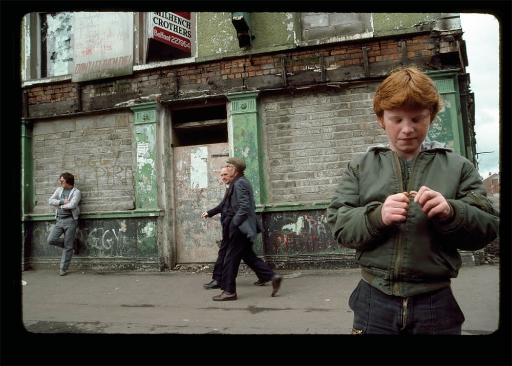 A young boy stands holding and observing a metal ring in his hands while men pass behind him. 