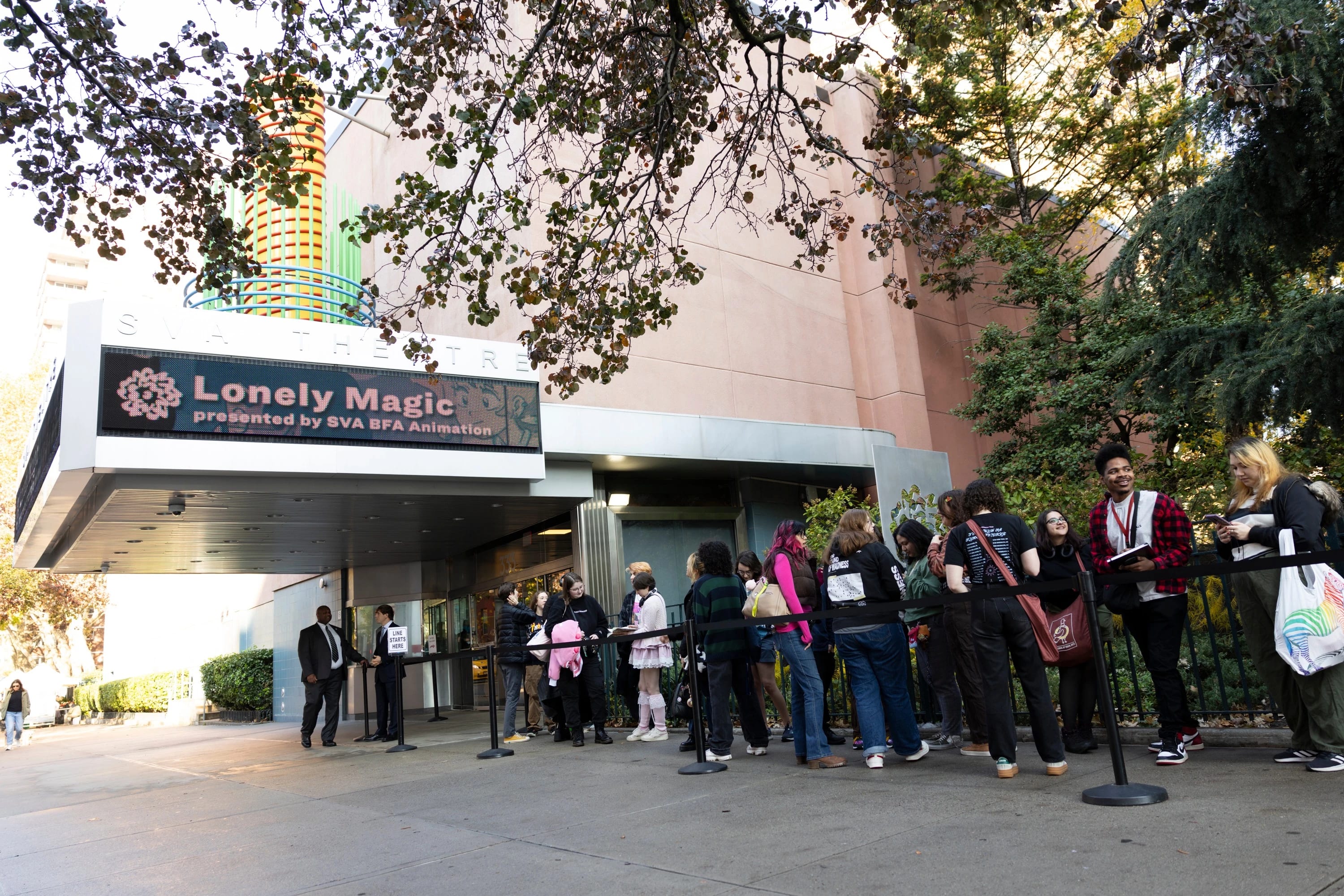 A line of SVA community members stands outside the SVA Theatre. Above the entrance, a large marquee sign displays the title ‘Lonely Magic.