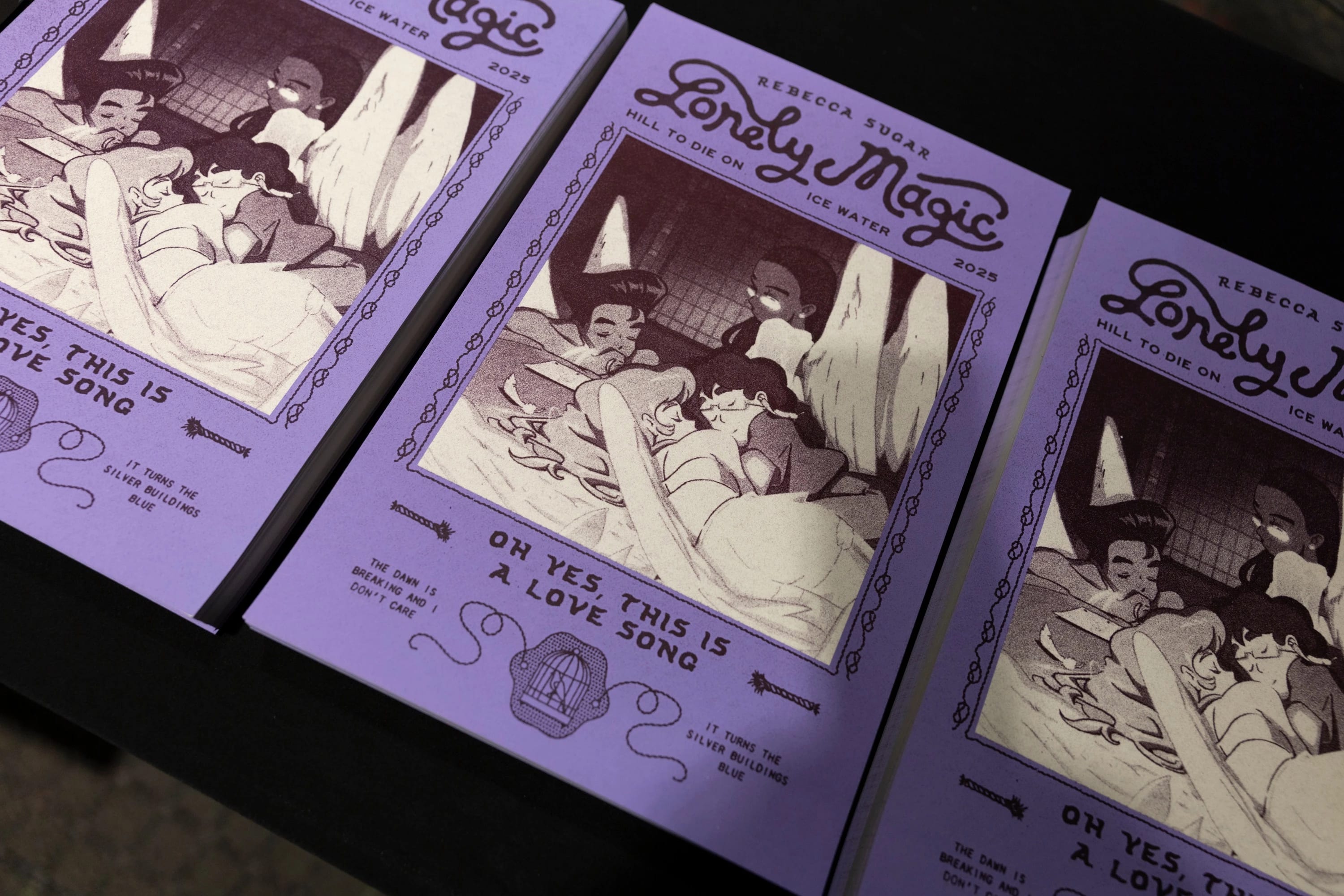 Zoomed-in shot of three lavender-colored posters titled “ Lonely Magic,” featuring an illustration of three angels.