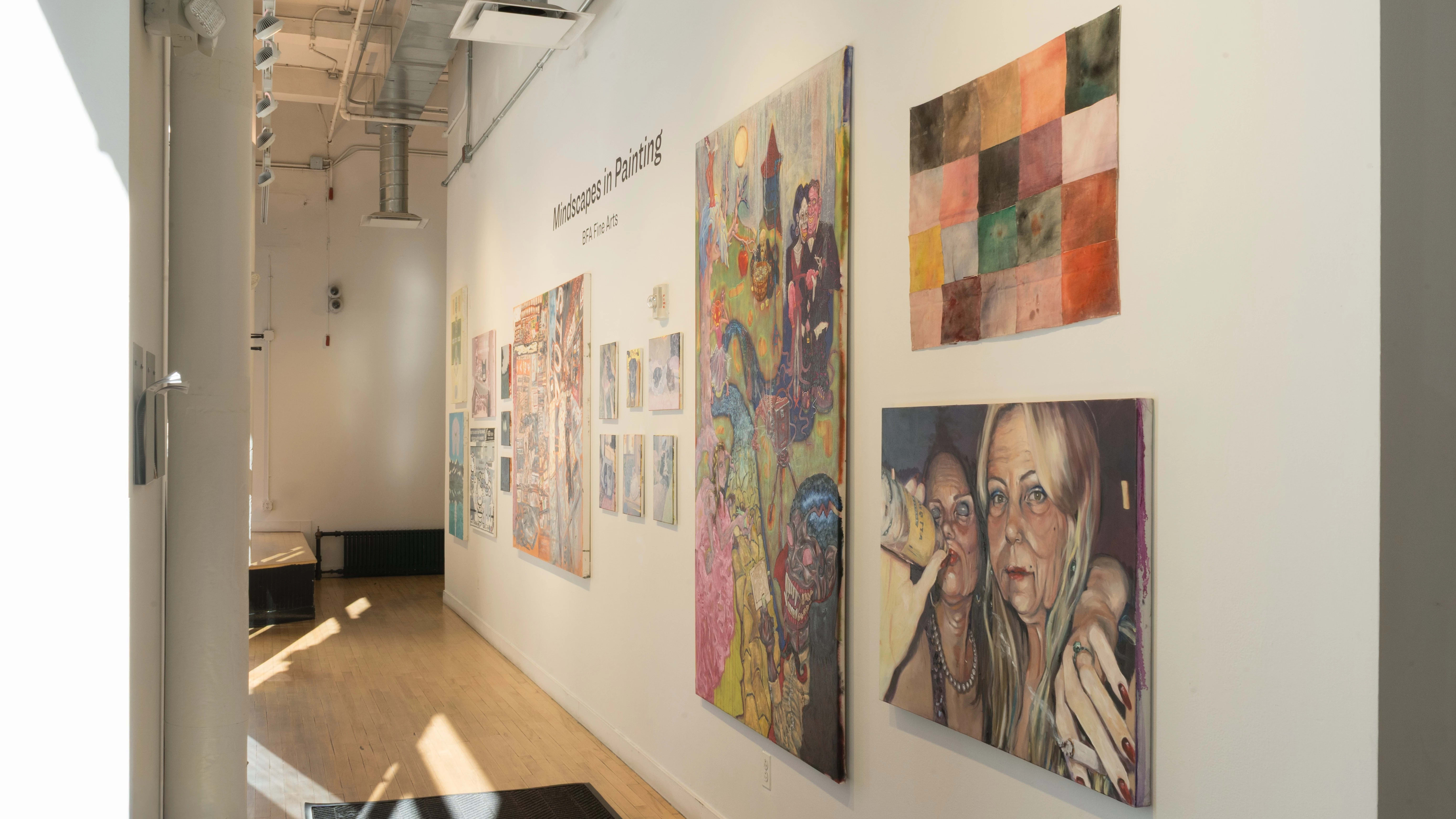 A long gallery wall displays paintings by several different artists, ranging from small to oversized.