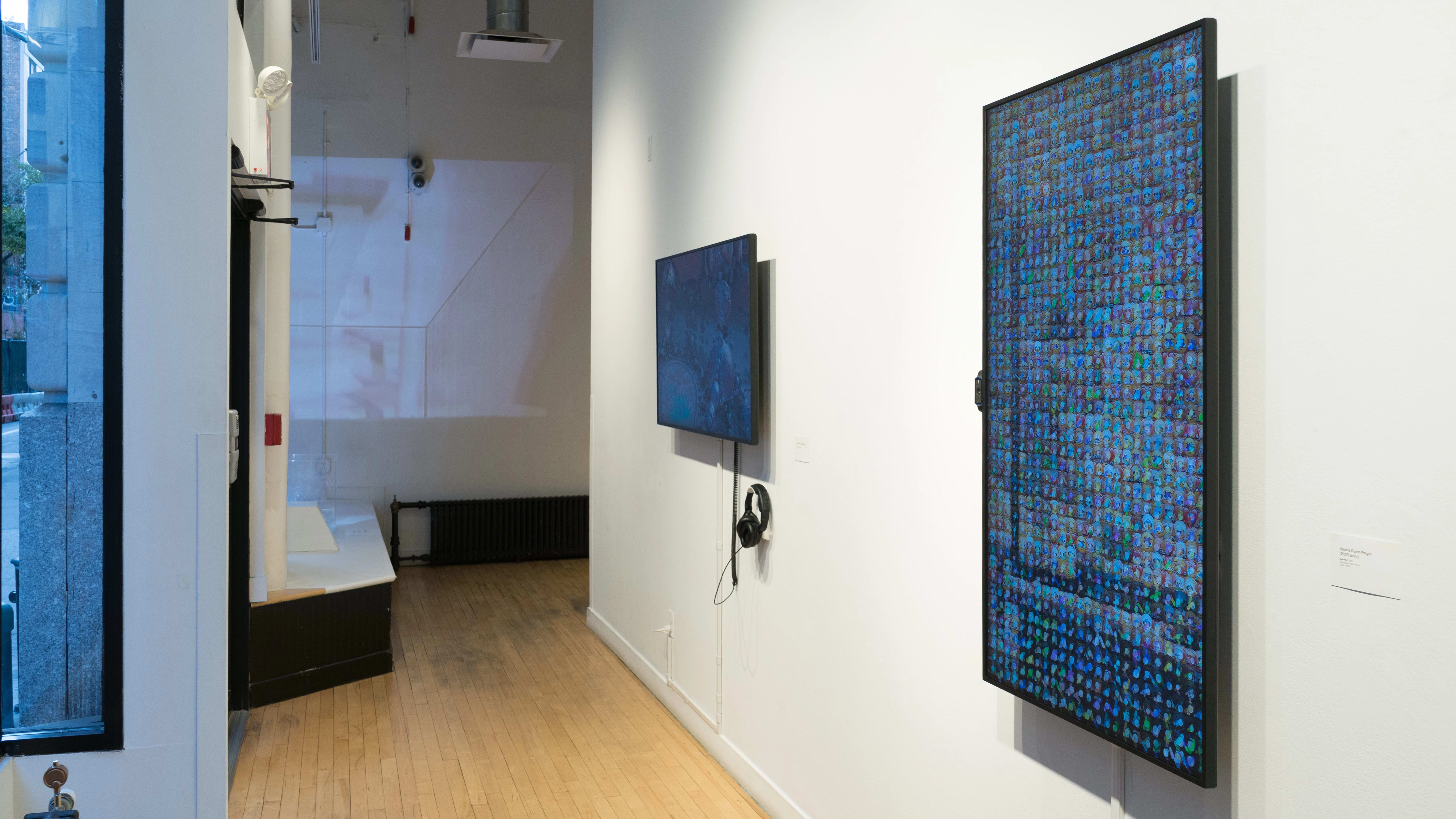 Towards the end of the hallway, a vertical monitor on the wall shows many small square images arranged all together. To its left, a horizontal monitor plays something else, and a projection on the far end shows a third thing.