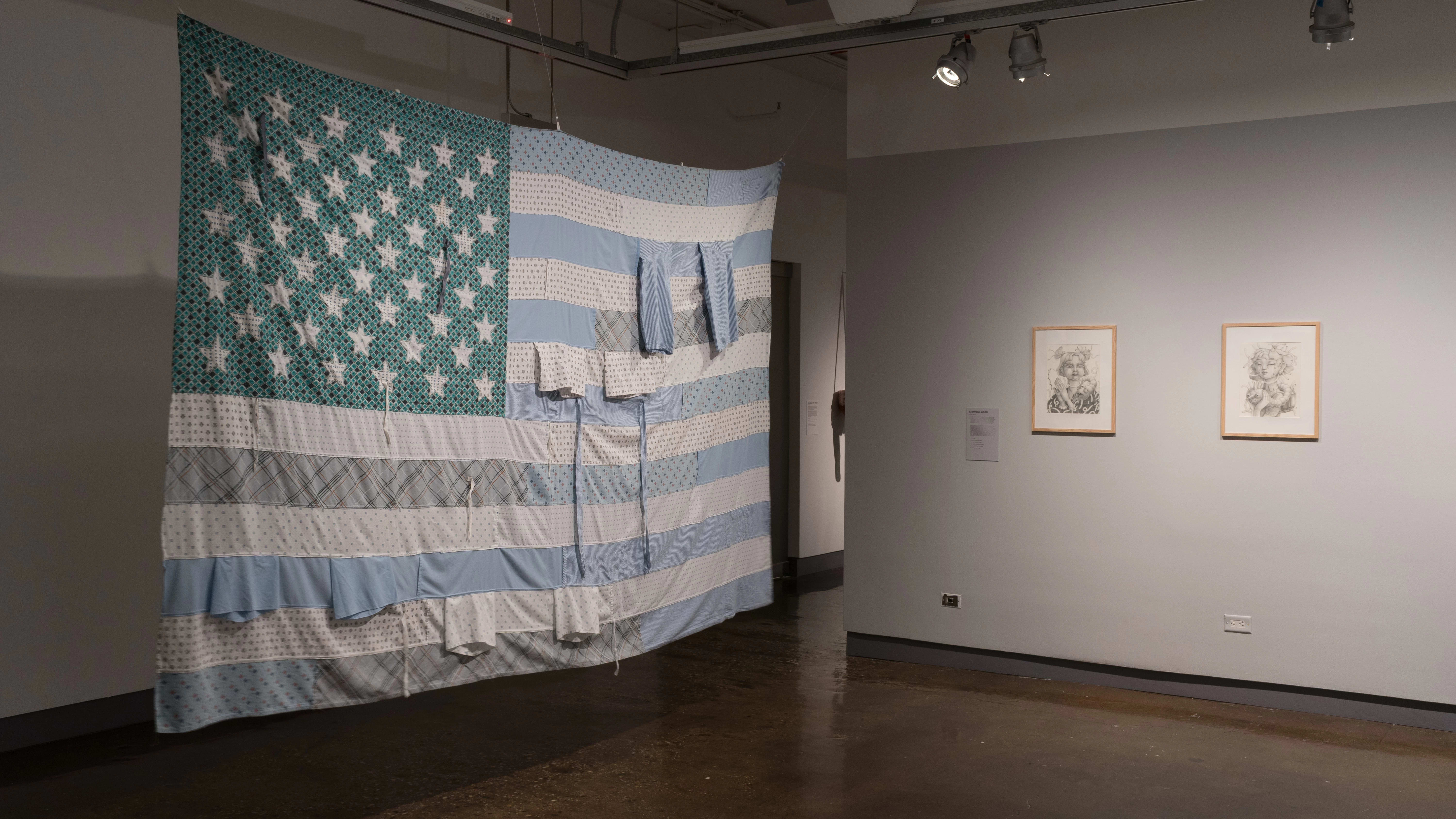 A large, light blue and turquoise colored American flag hangs from the ceiling. Two framed illustrations hang to the right.
