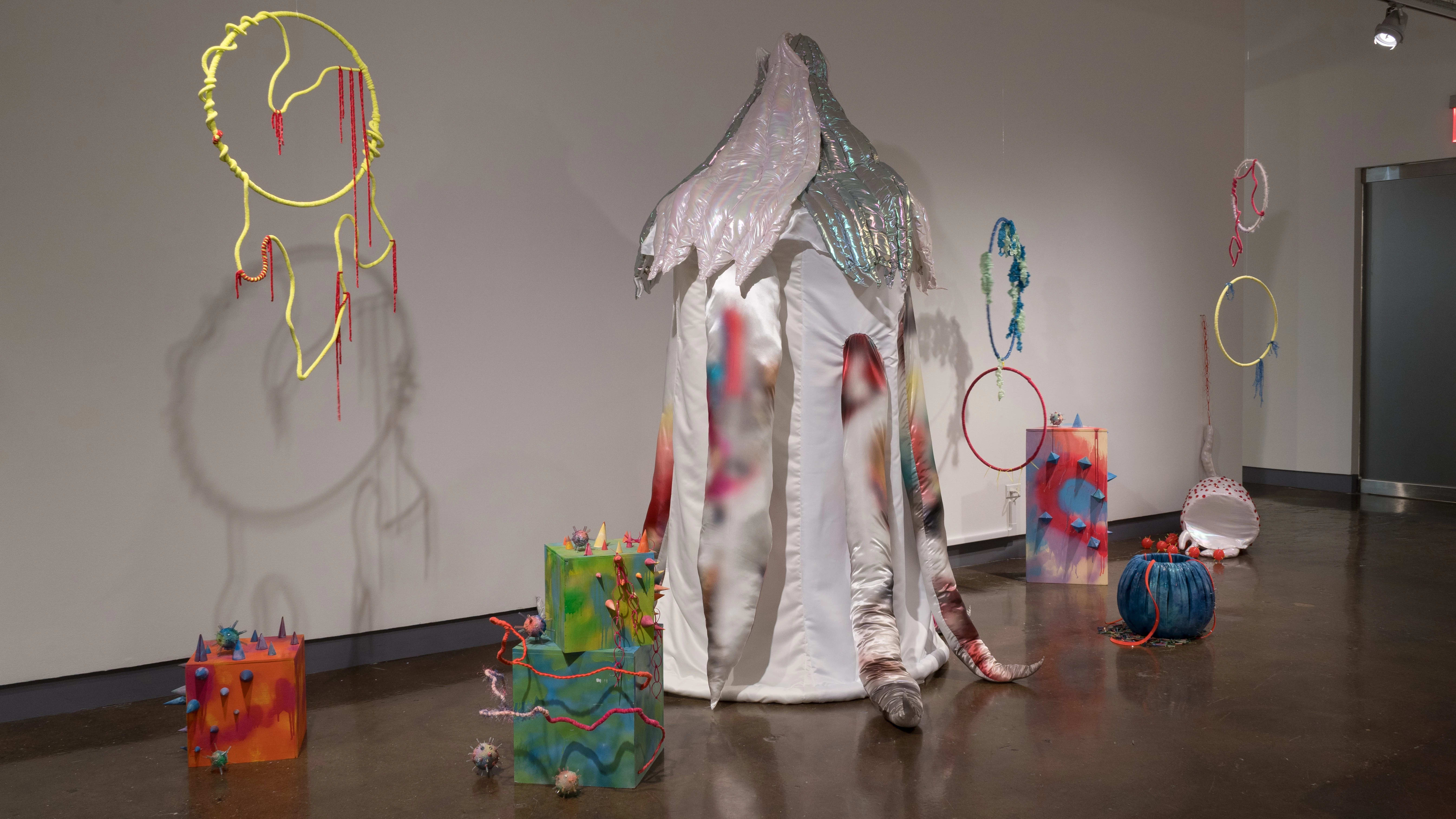 A wall with clown-themed sculptural pieces, including a tent and circus rings made of fabric and other soft materials.