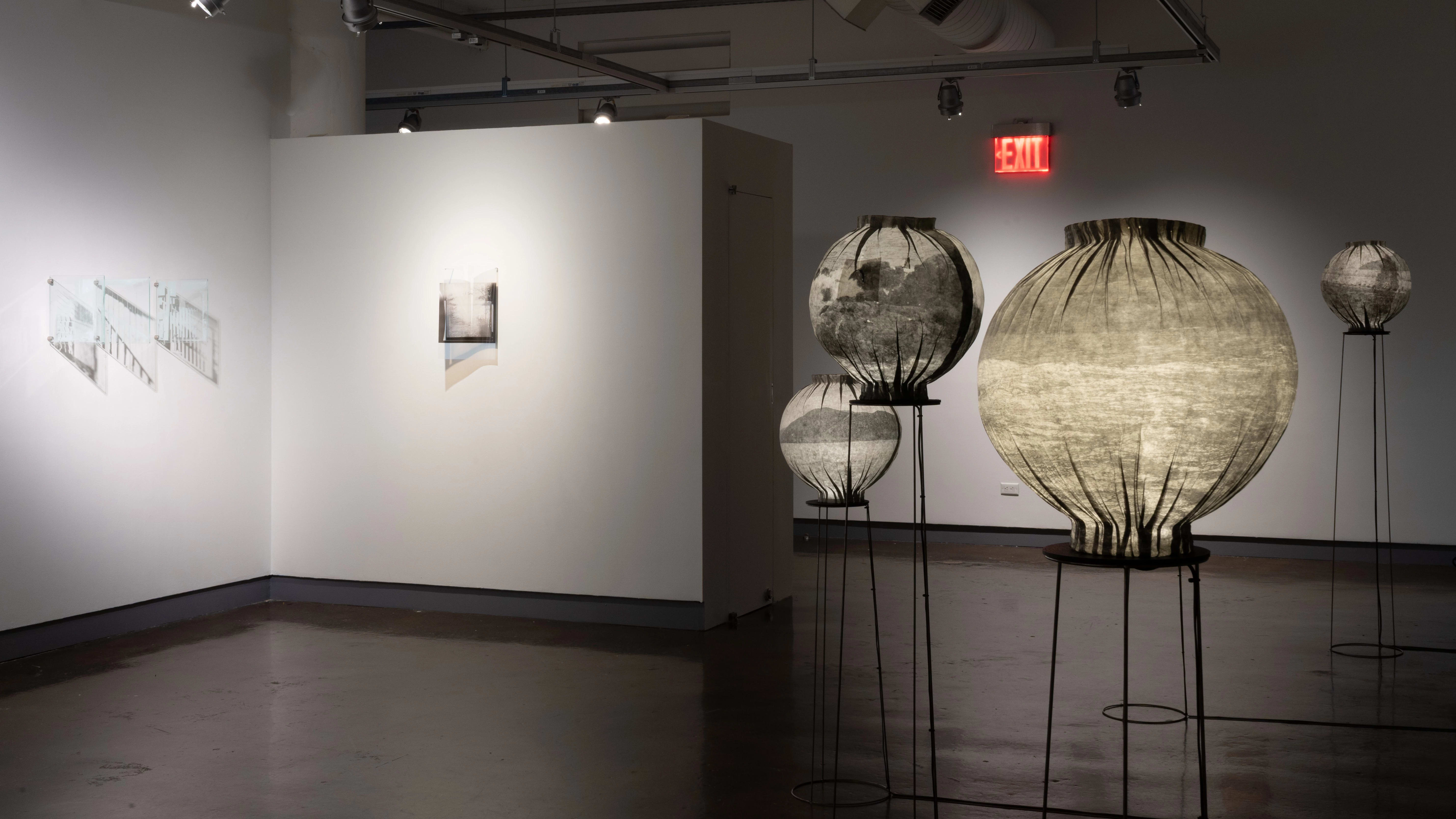 The third gallery with photographs printed on glass on the left wall and paper lanterns on wire pedestals on the right.