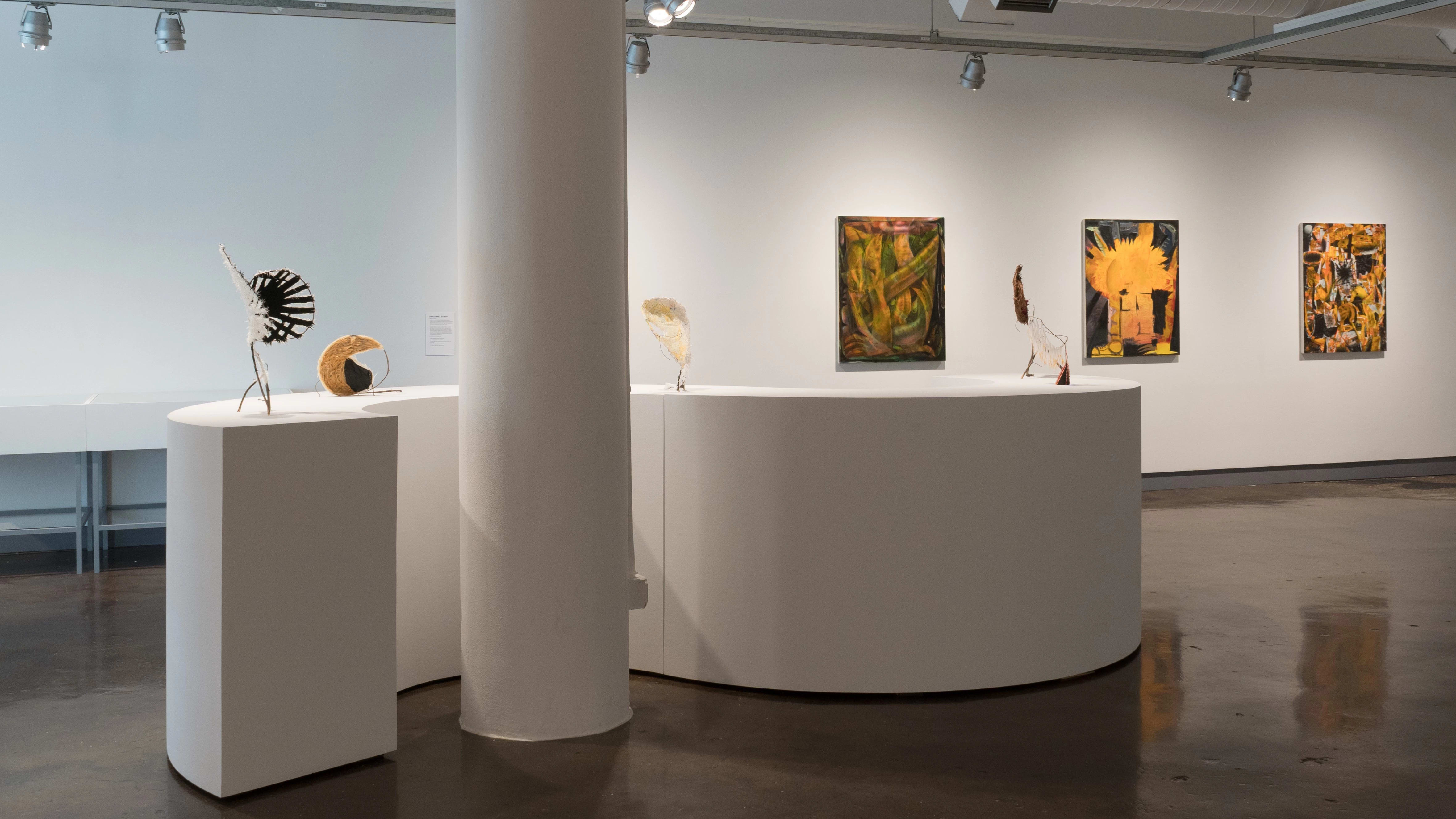 The first gallery with an S-shaped table depicting several sculptural pieces, with paintings on the wall behind.