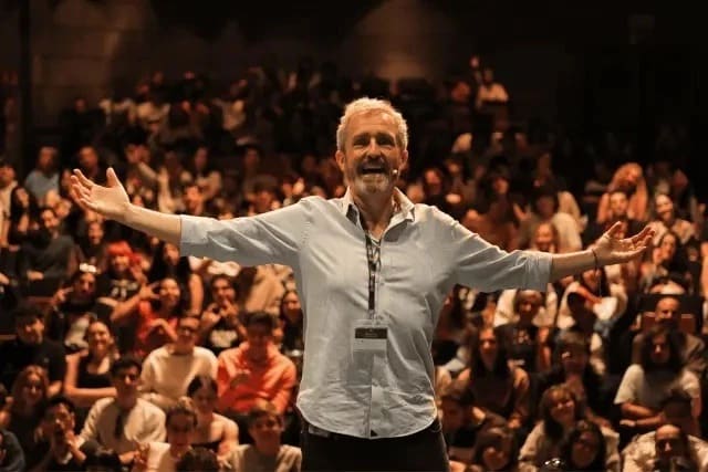 Man stands with arms open, smiling in front of a crowd of people