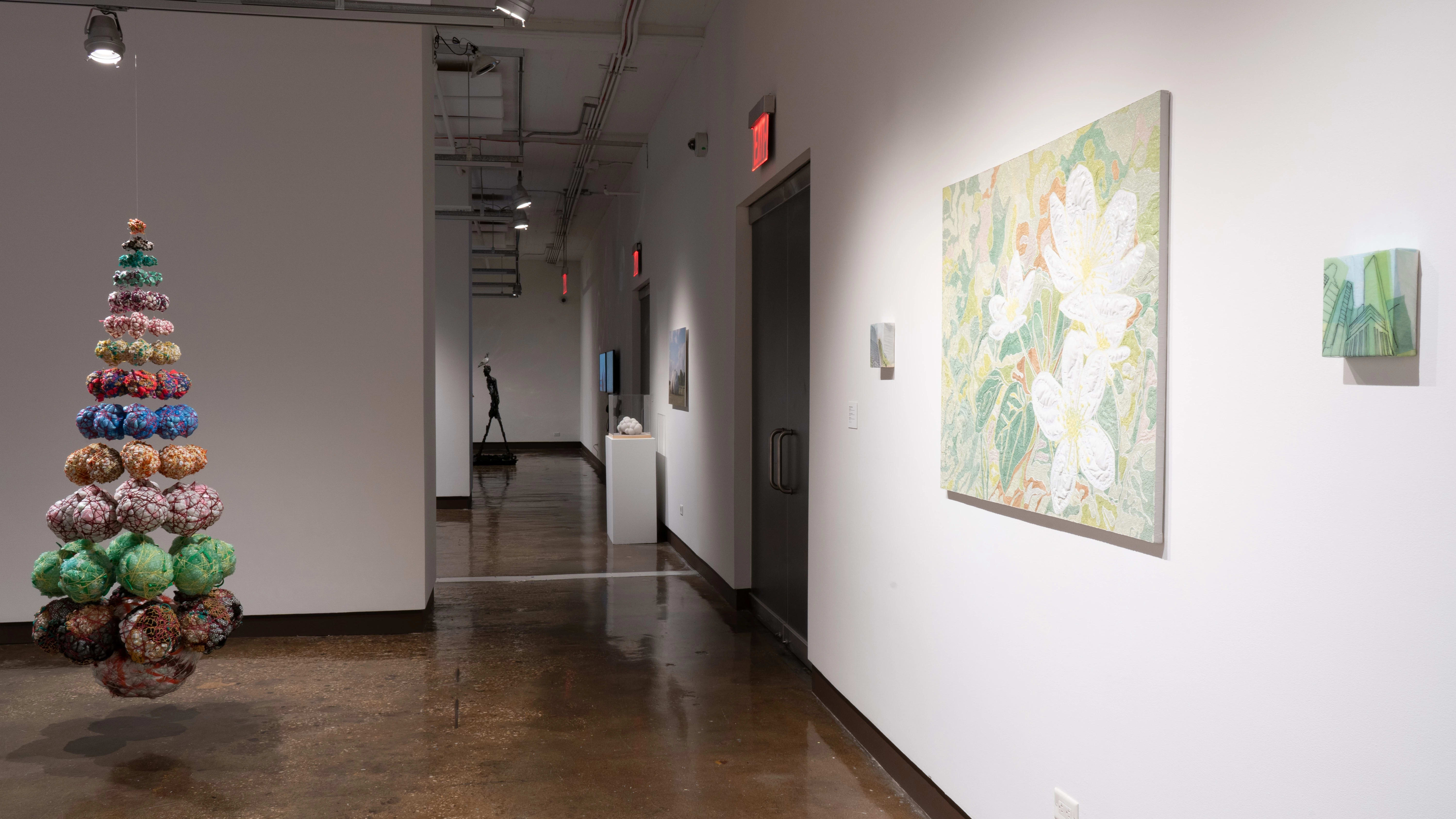 Looking down the hall towards gallery one, the suspended cone shape and a canvas of embroidered plastic flowers are visible.
