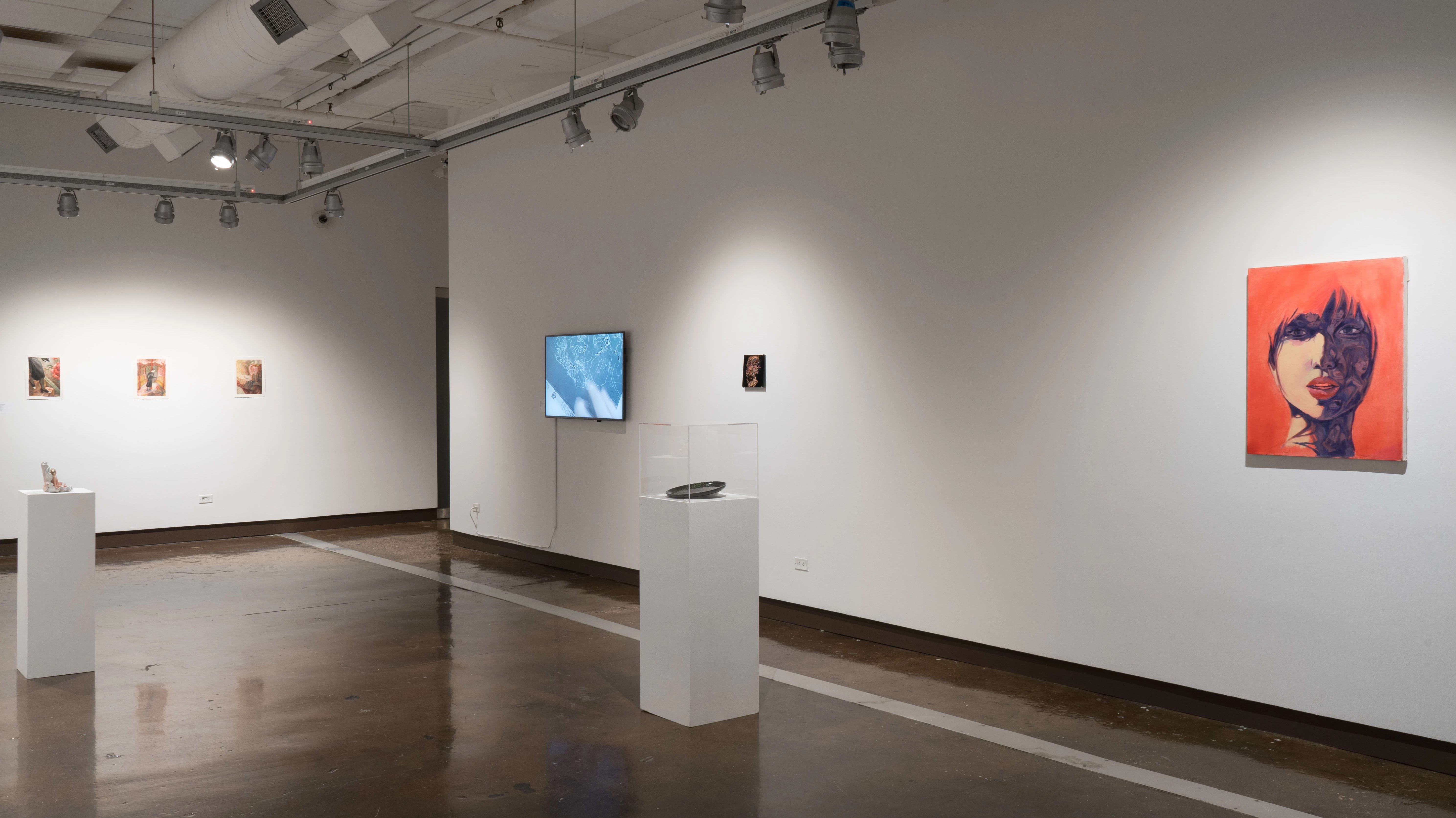 Pedestals holding a plate and ceramic sculptures sit in the middle of the second gallery space. On the furthest wall to the left, there are three watercolor-on-paper pieces. On the wall to the right, a screen is displayed playing videos of an art making process. A small painting hangs next to the displayed video, and an orange and purple oil painting hangs at the very end of the right wall.