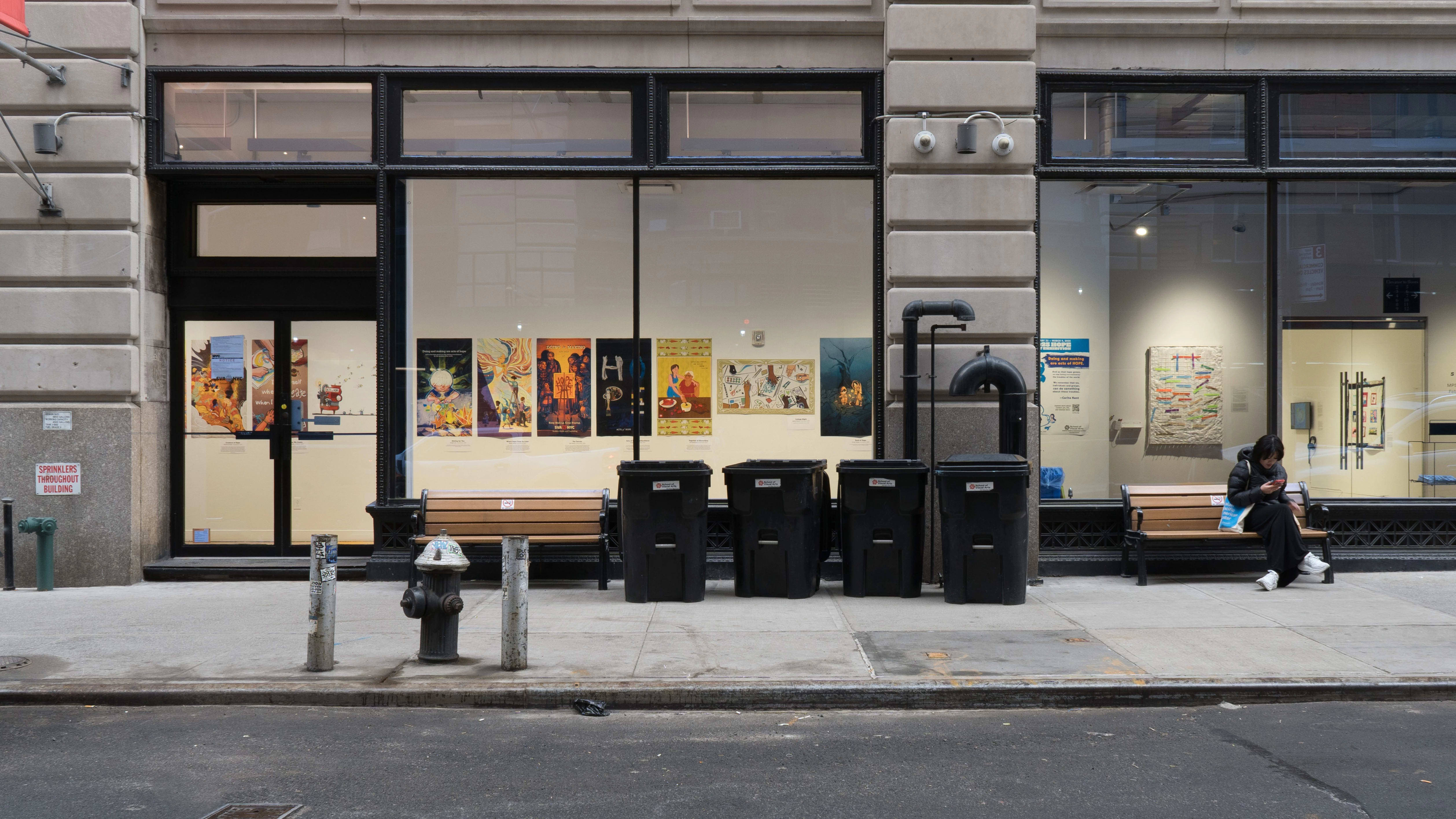 View from the street of the SVA Flatiron Windows, showing many colorful posters with themes of hope lining the wall.