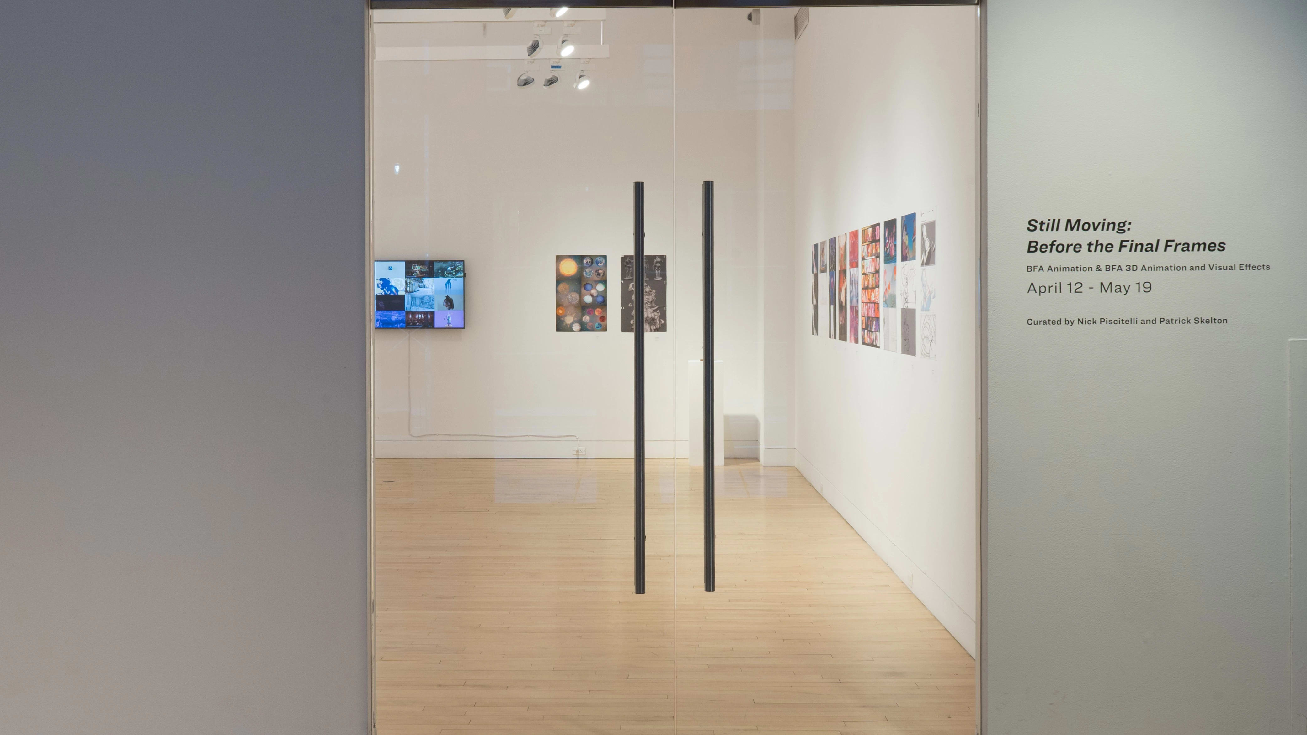 A view of the glass gallery doors at the SVA Flatiron Gallery, with the title to the right in vinyl, and multiple prints and a monitor visible through the glass.