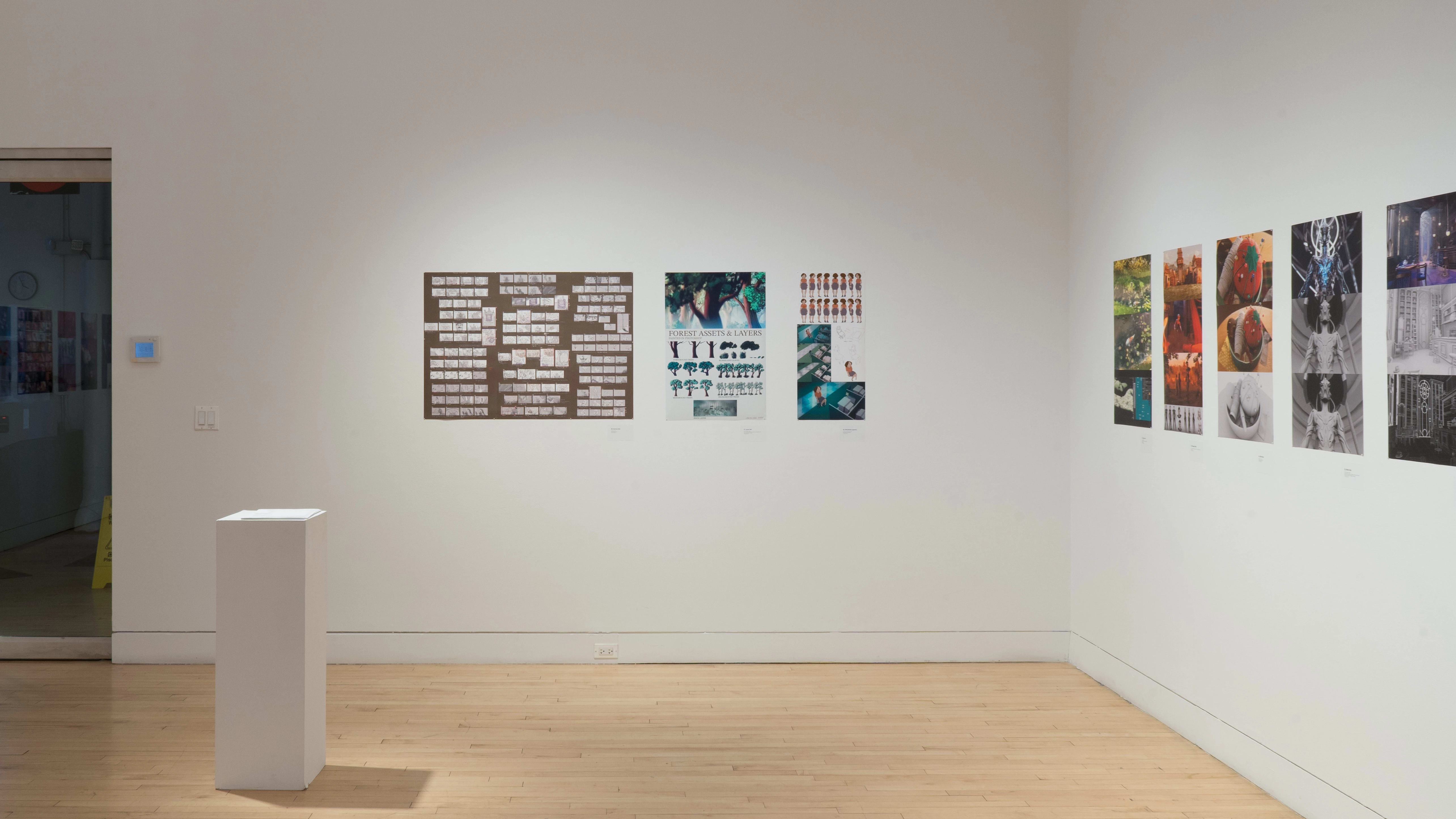 A stright shot of the SVA Flatiron Gallery's south and west walls, showing many colorful prints by BFA Animation students pinned up; some paper sits atop a pedestal in the left foreground. The glass doors are visible in the back left.